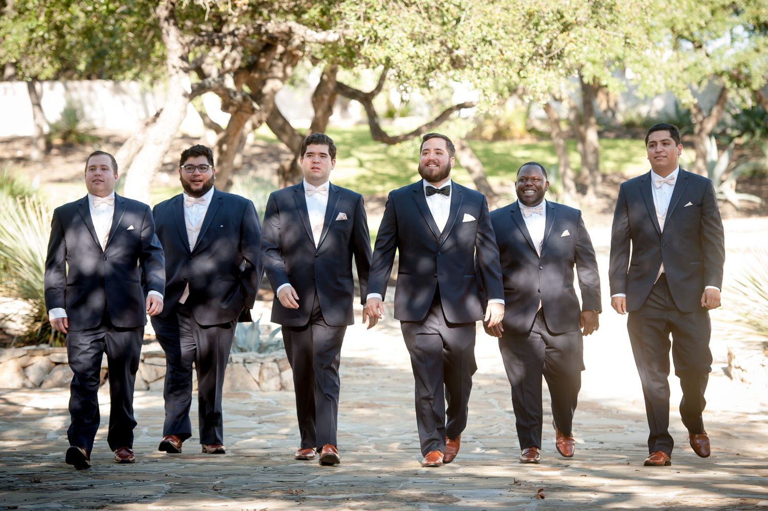 Groomsmen walking in synchronized motion wearing formal black suits outdoors.