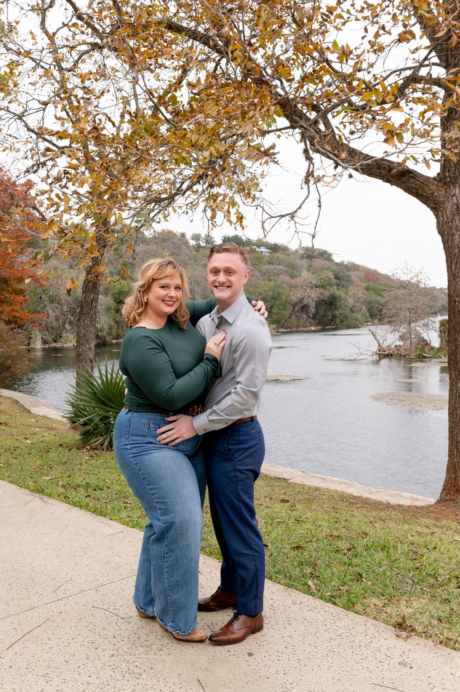 Couple's engagement session by the water with golden autumn leaves overhead.