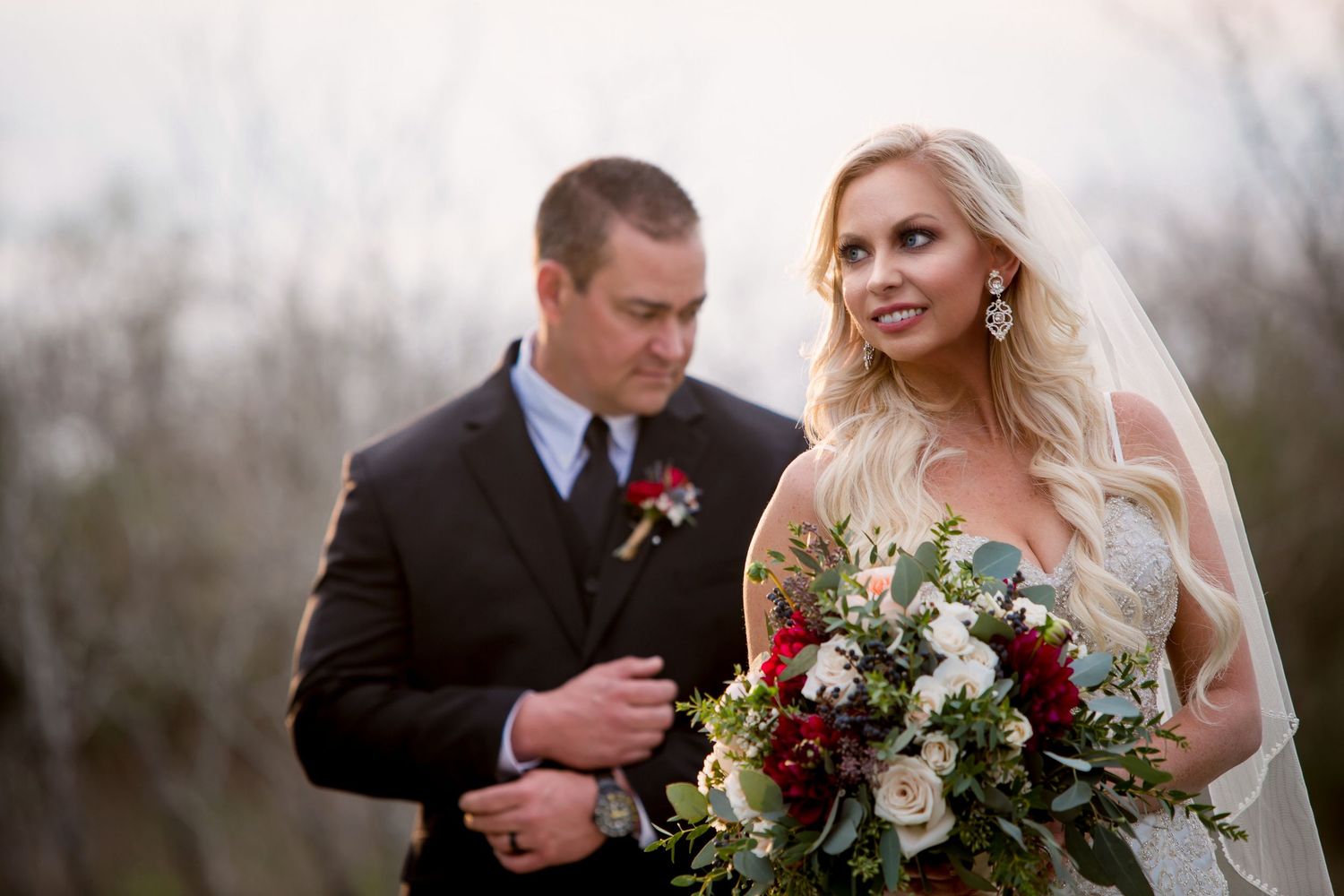 Wedding party members hold elegant floral bouquets during outdoor ceremony.