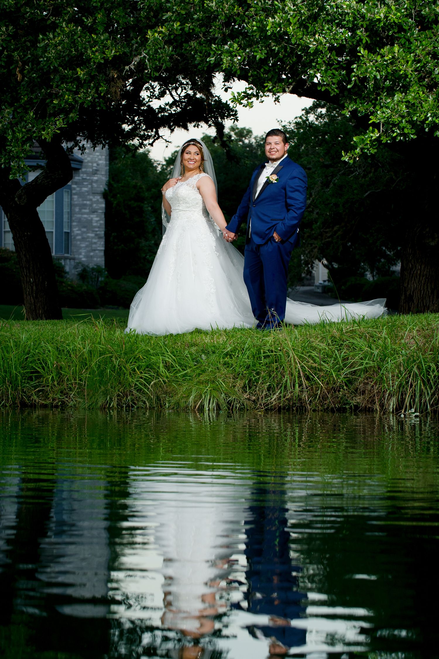 Wedding couple poses by reflective pond with lush greenery creating romantic garden setting.