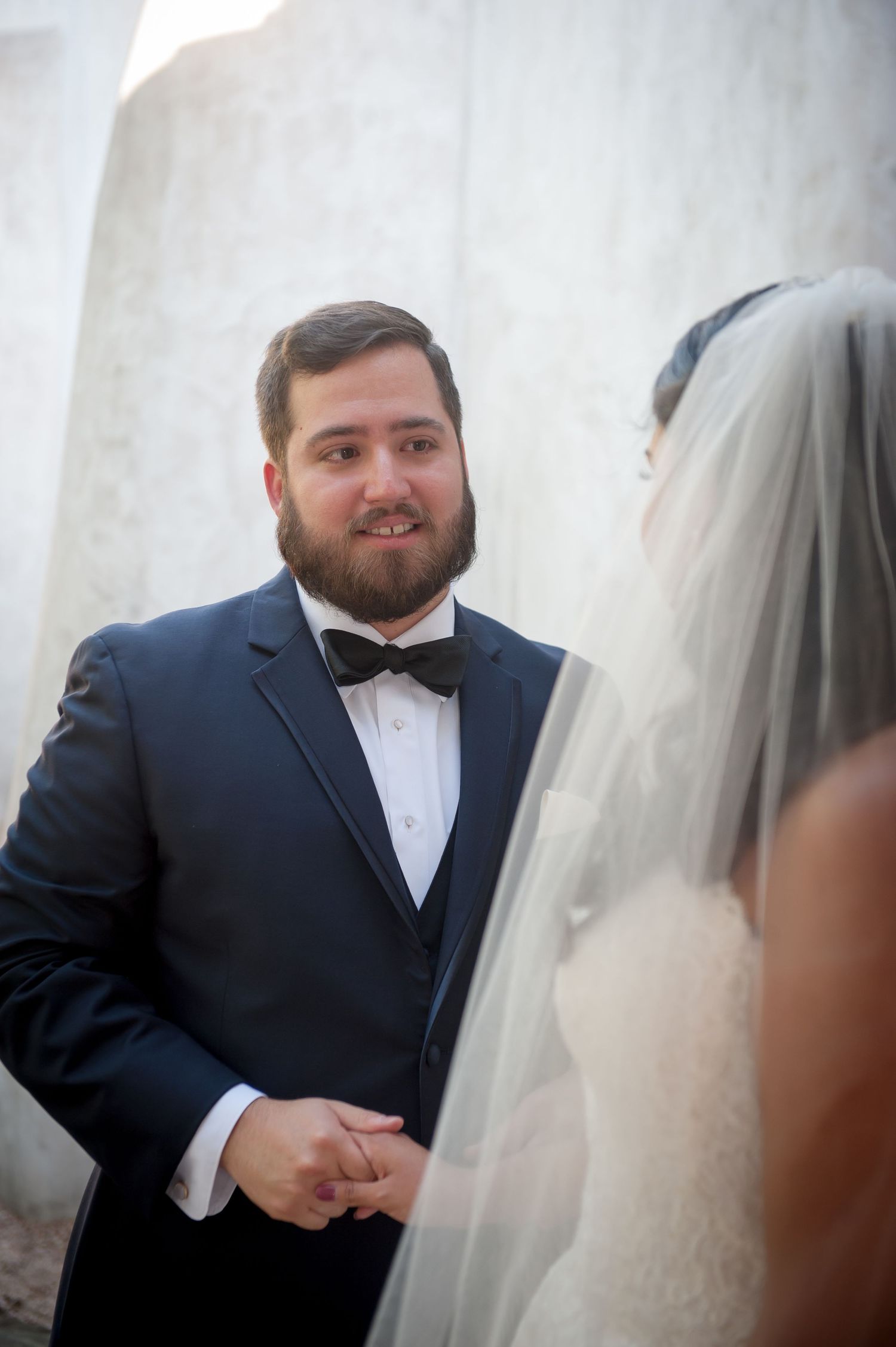 A groom in a navy suit and white tie reacts emotionally during a first look moment at a wedding.