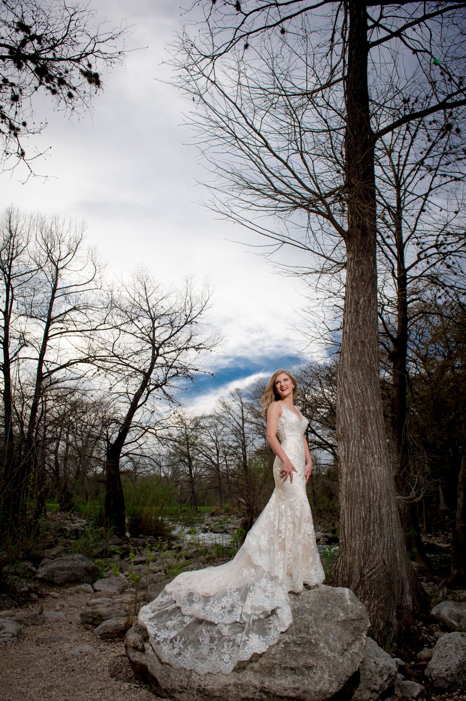 Ethereal bridal portrait among bare winter trees on rocky outdoor setting.