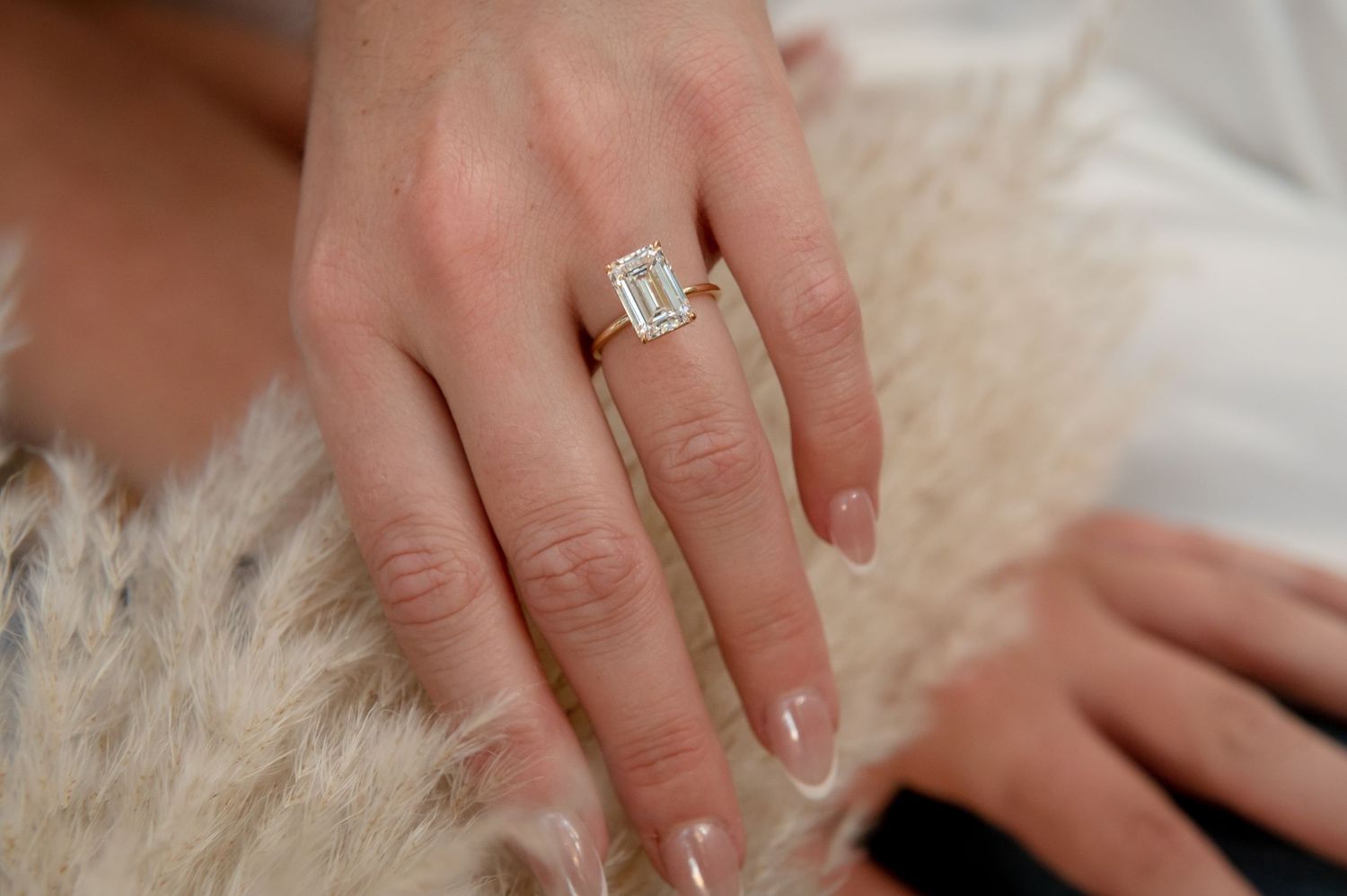 Close-up shot of an emerald cut engagement ring on a hand resting on white fur.