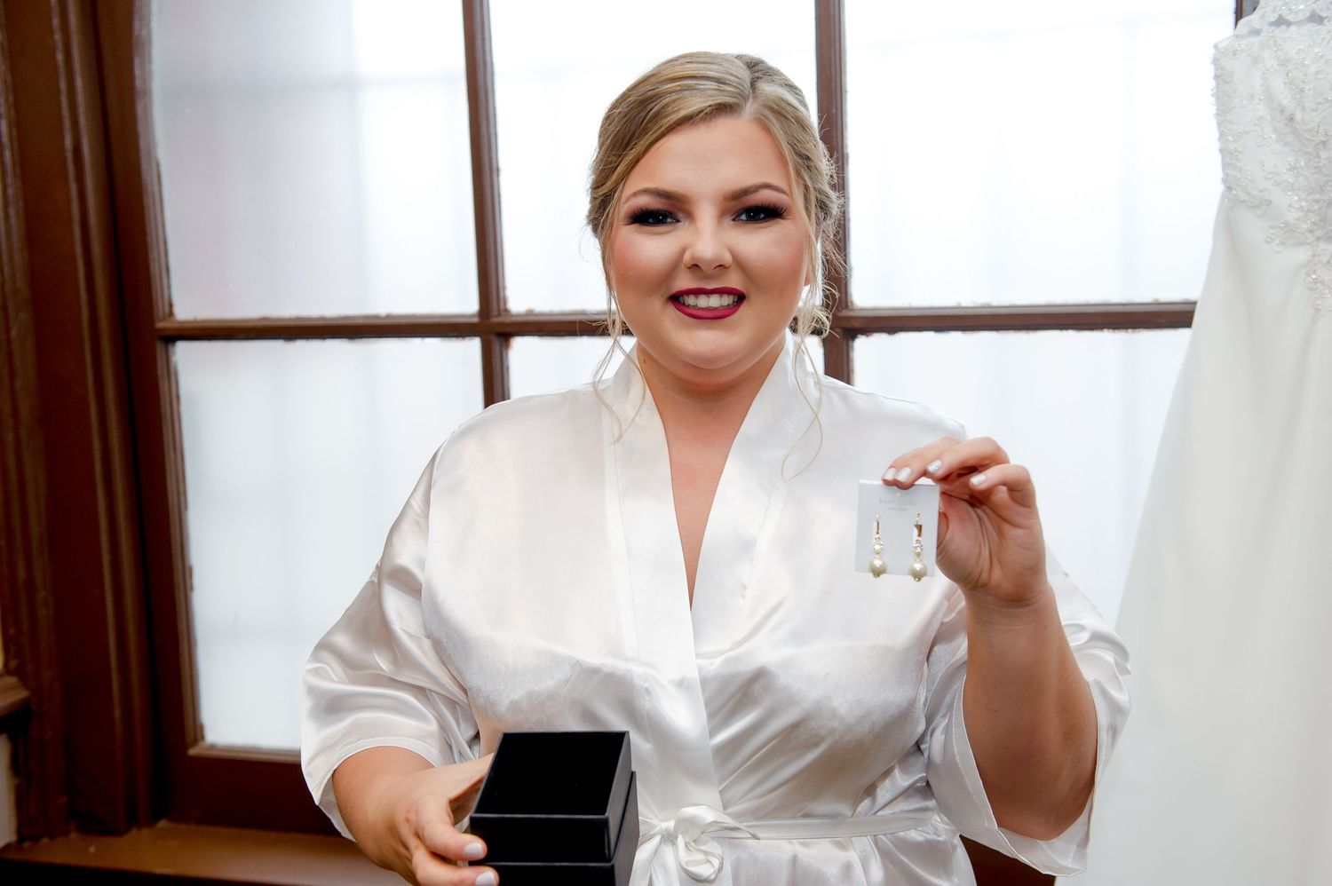 Person in white robe getting ready with wedding dress visible in background.