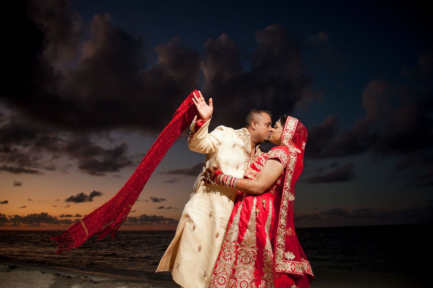 Romantic moment between couple in traditional Indian wedding attire at sunset.