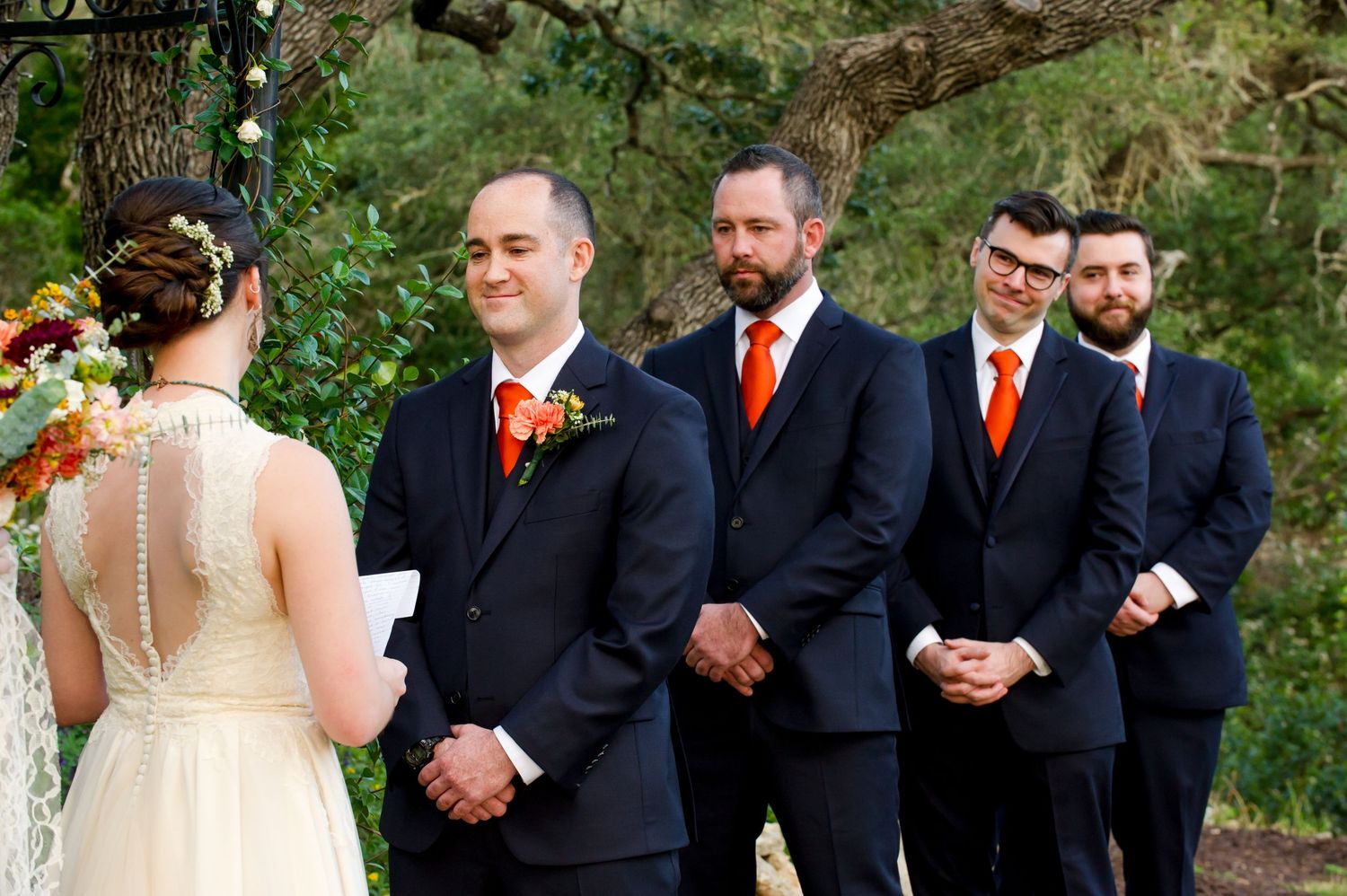 Wedding party in navy suits and formal attire lined up outdoors during ceremony.