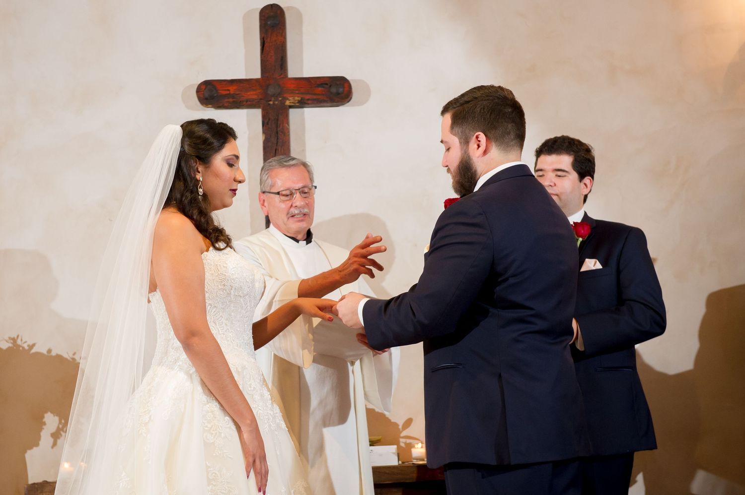 Wedding ceremony taking place in a traditional church sanctuary with wooden cross and wall sconces.