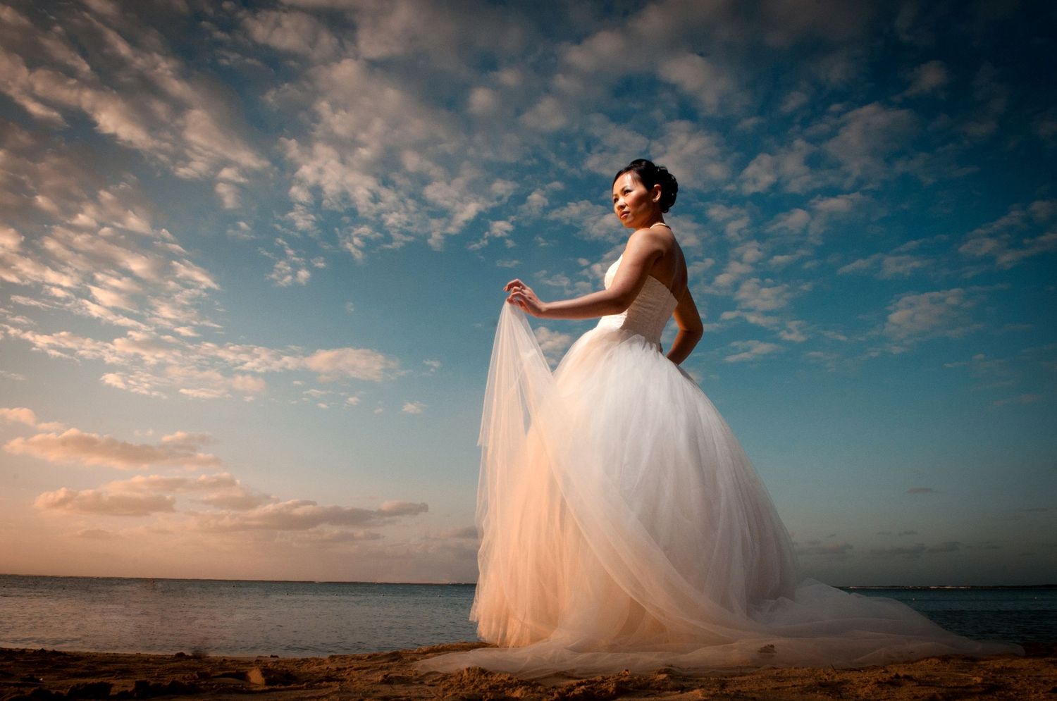 Dramatic sunset silhouettes wedding couple in flowing dress against cloudy sky.