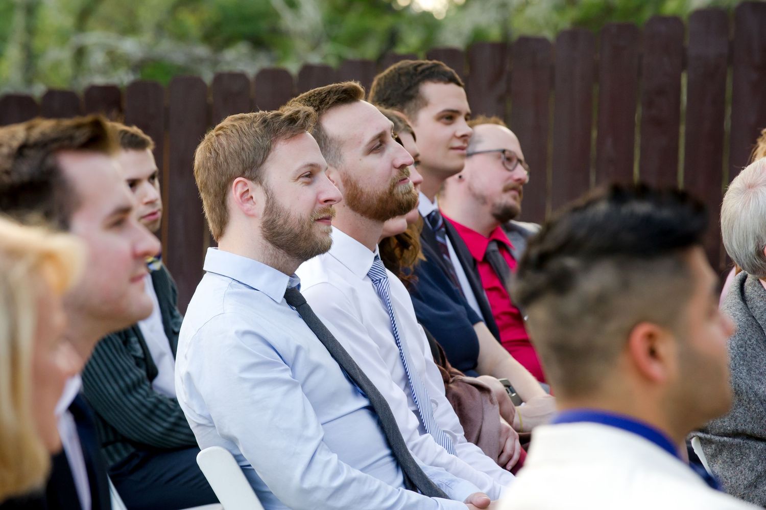 Wedding guests seated outdoors watching ceremony with attentive expressions.