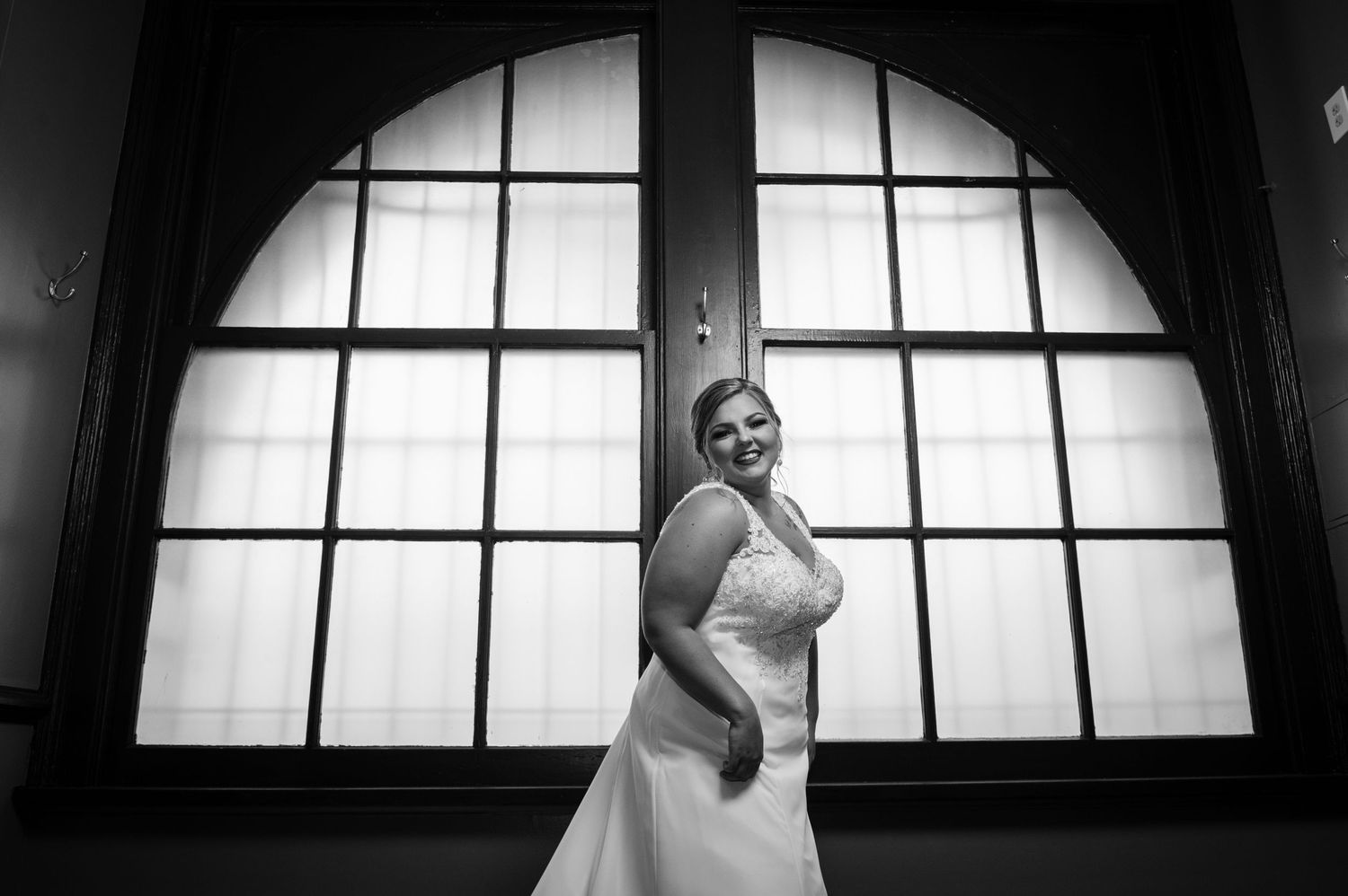 A bride poses in front of an arched window in dramatic black and white lighting.