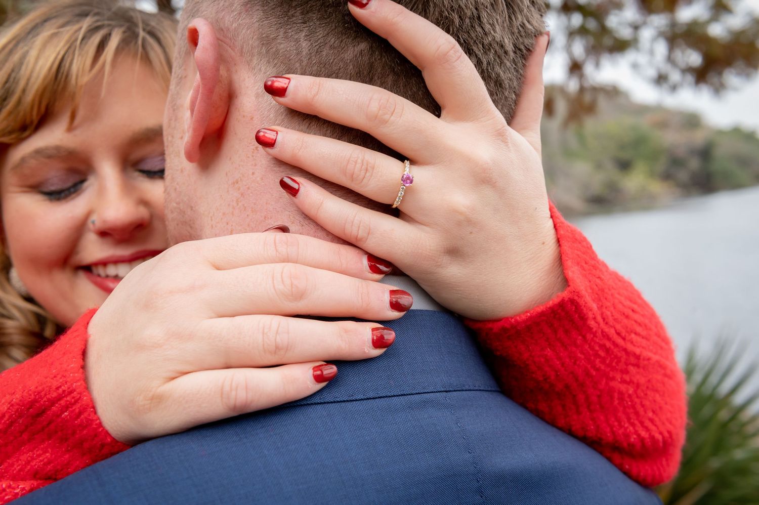 Close-up of hands with red nail polish and an engagement ring during an embrace.