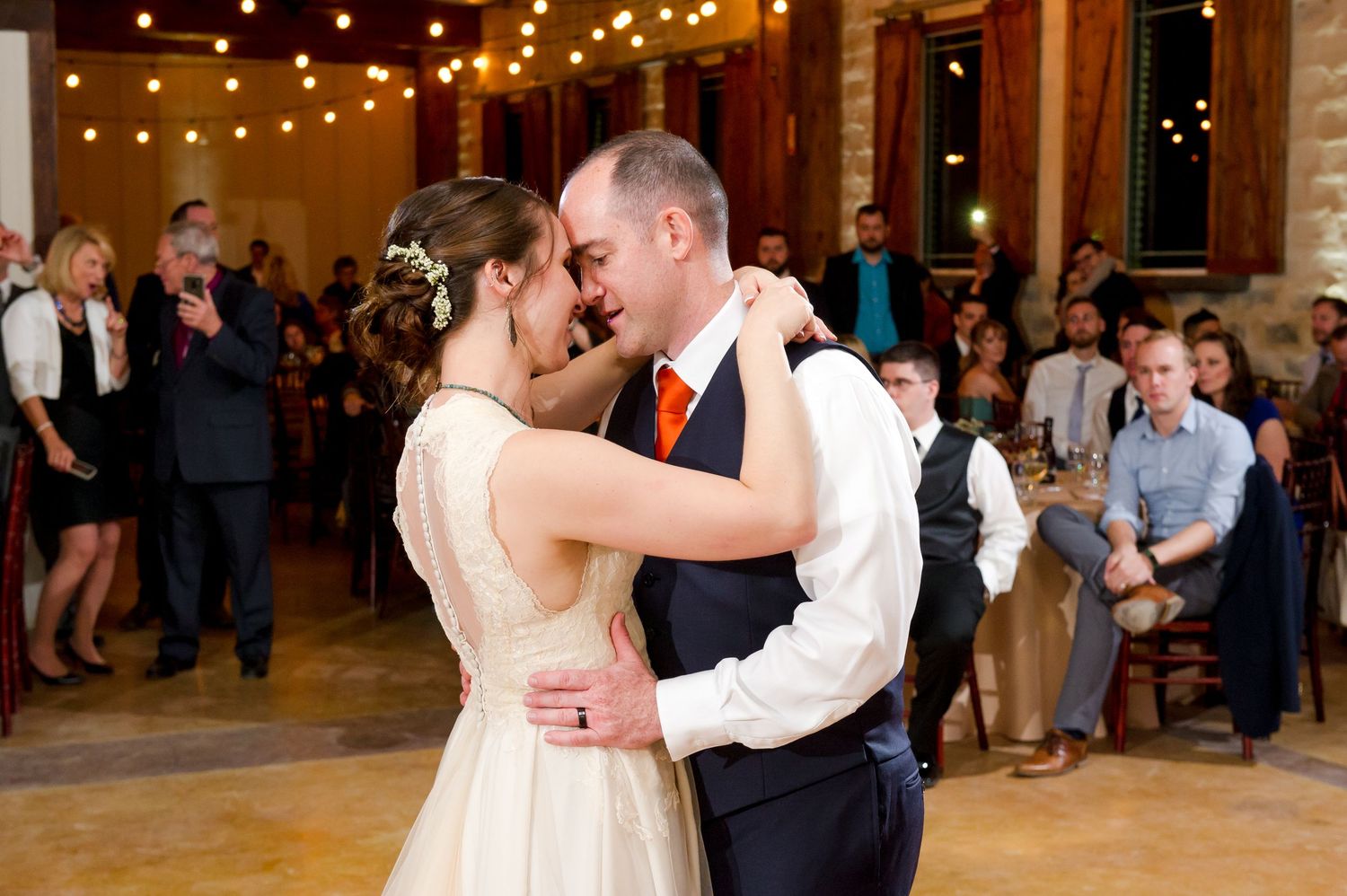 Couples share their first dance under warm string lights at an indoor wedding reception.
