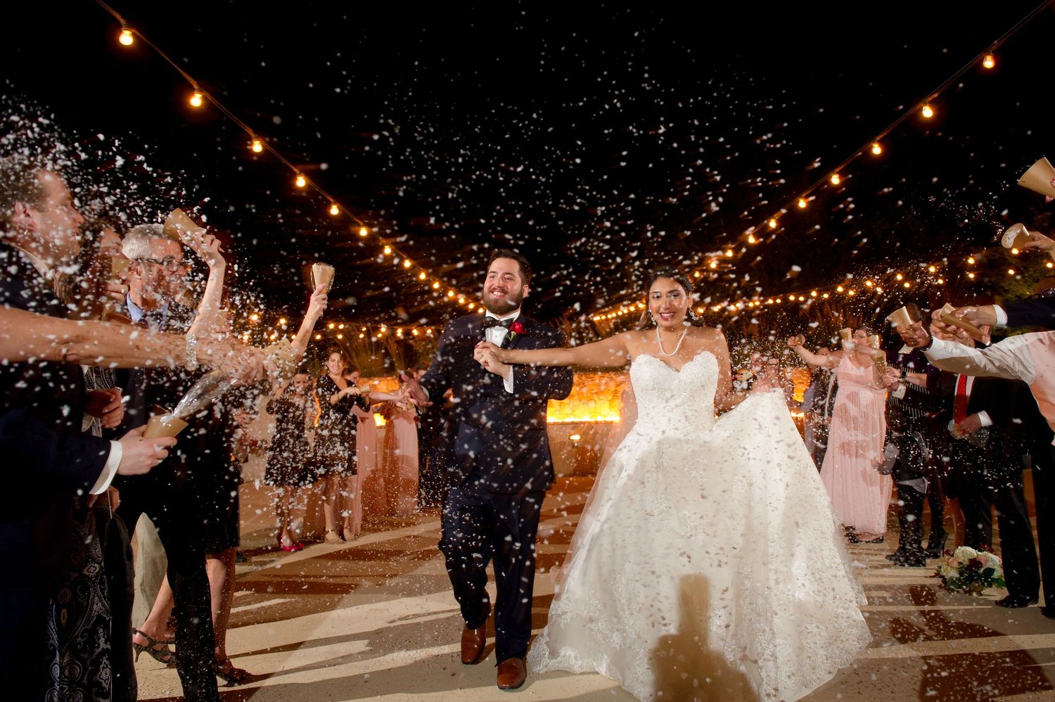 Wedding guests celebrate under twinkling string lights during an outdoor evening reception.