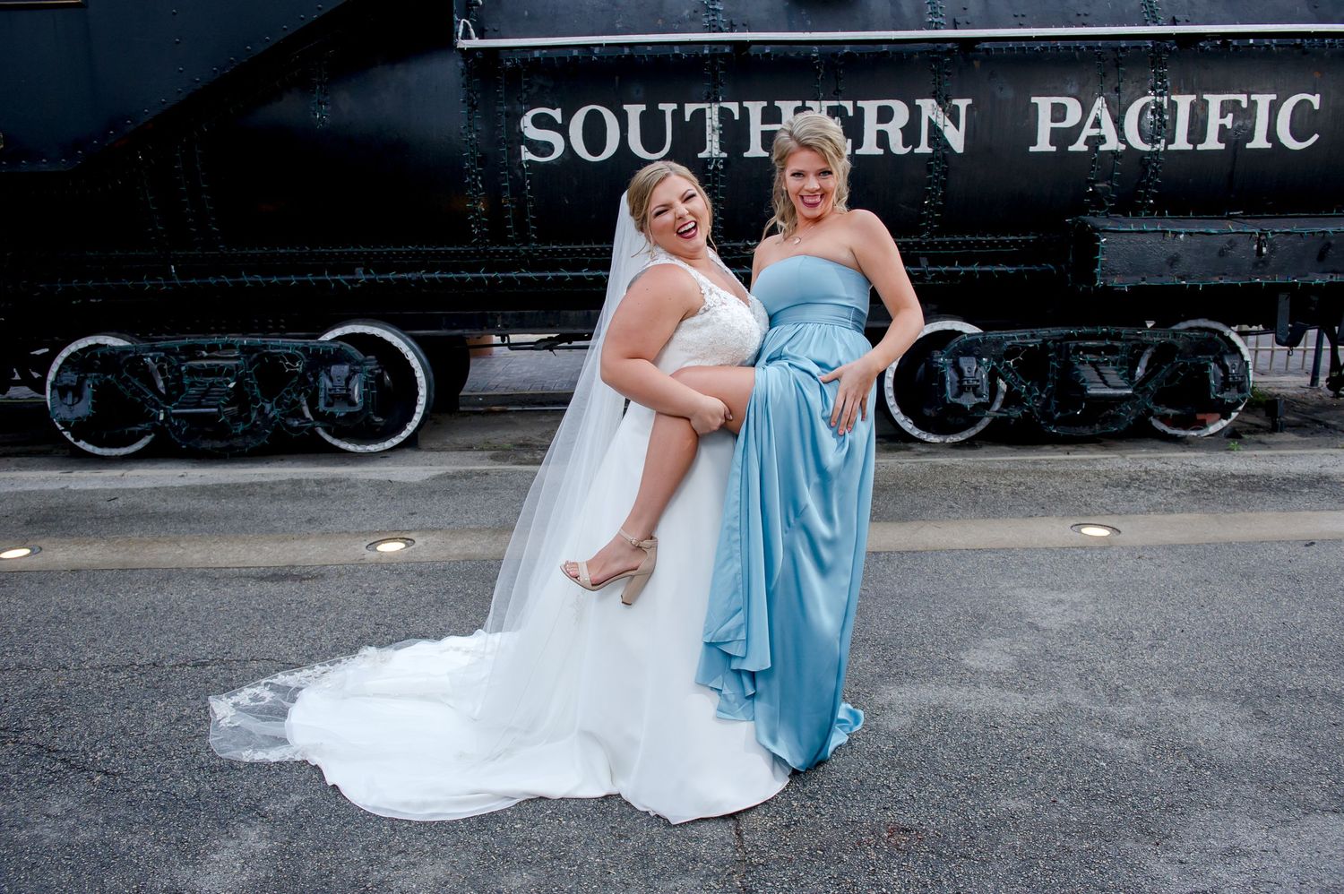 Bridal party members pose creatively along vintage train tracks in blue and white attire.