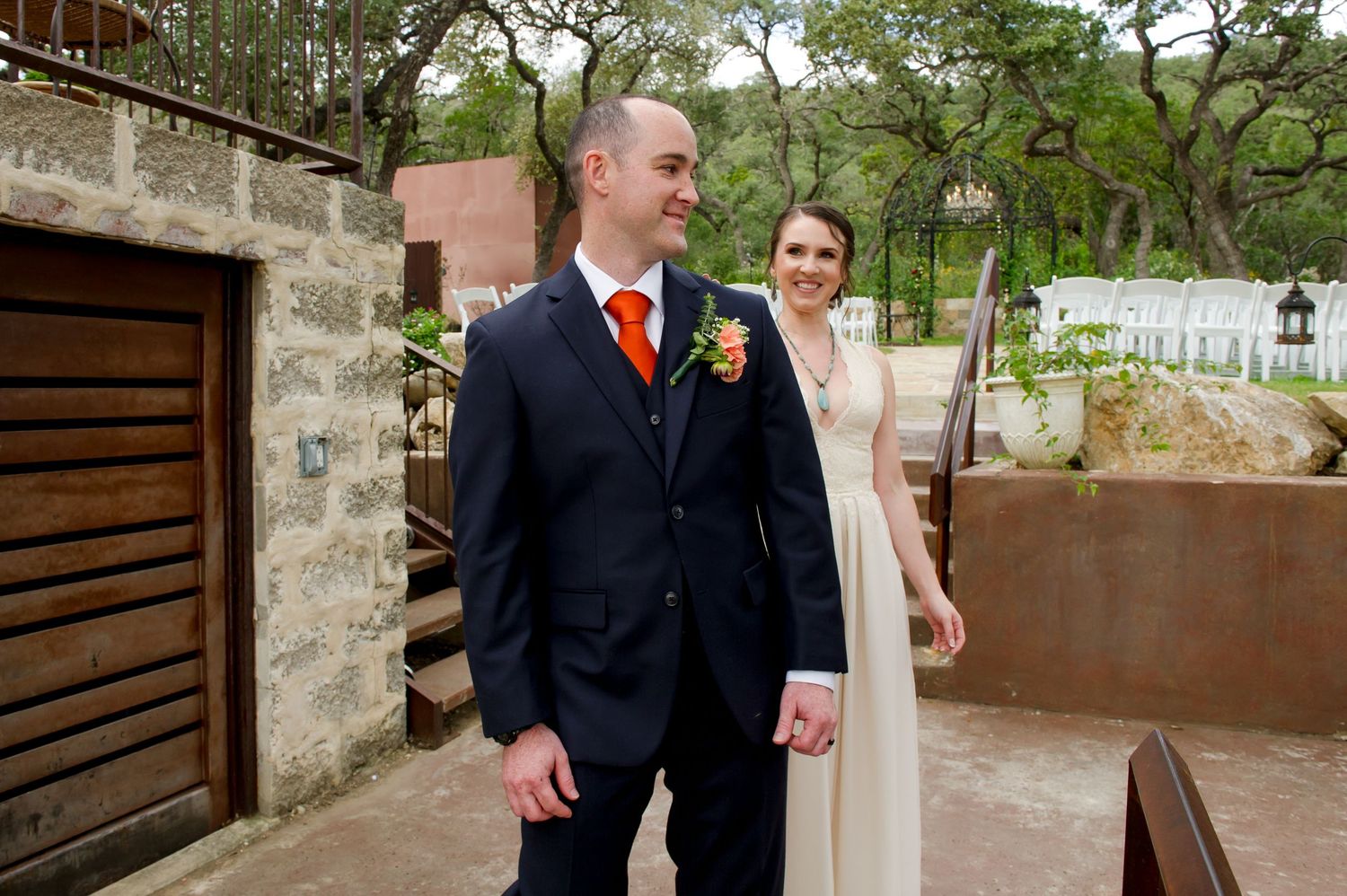 Wedding party members walk along a rustic stone pathway in formal attire on a sunny day.
