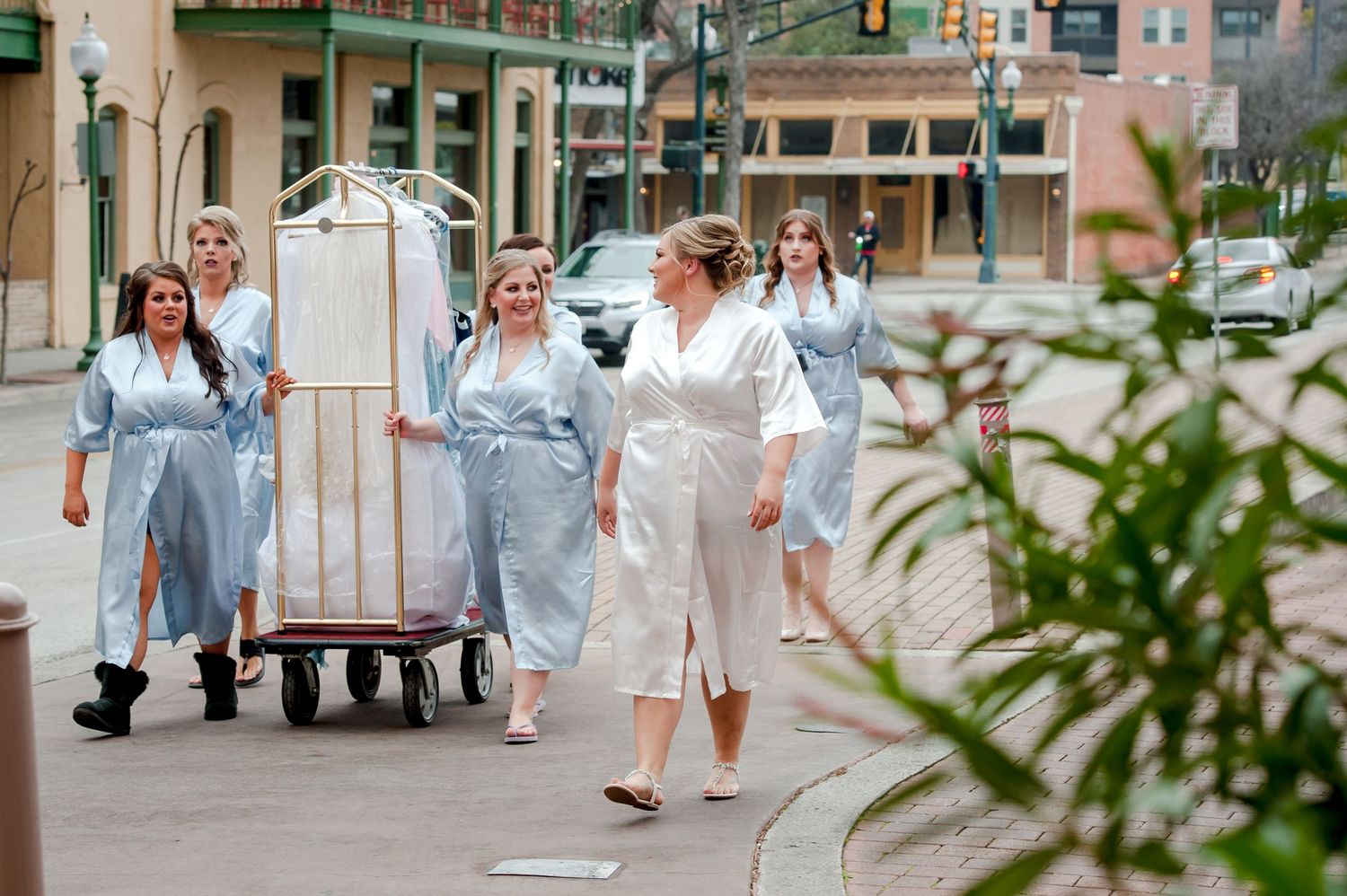 Wedding party members in light blue dresses walking along a city sidewalk.