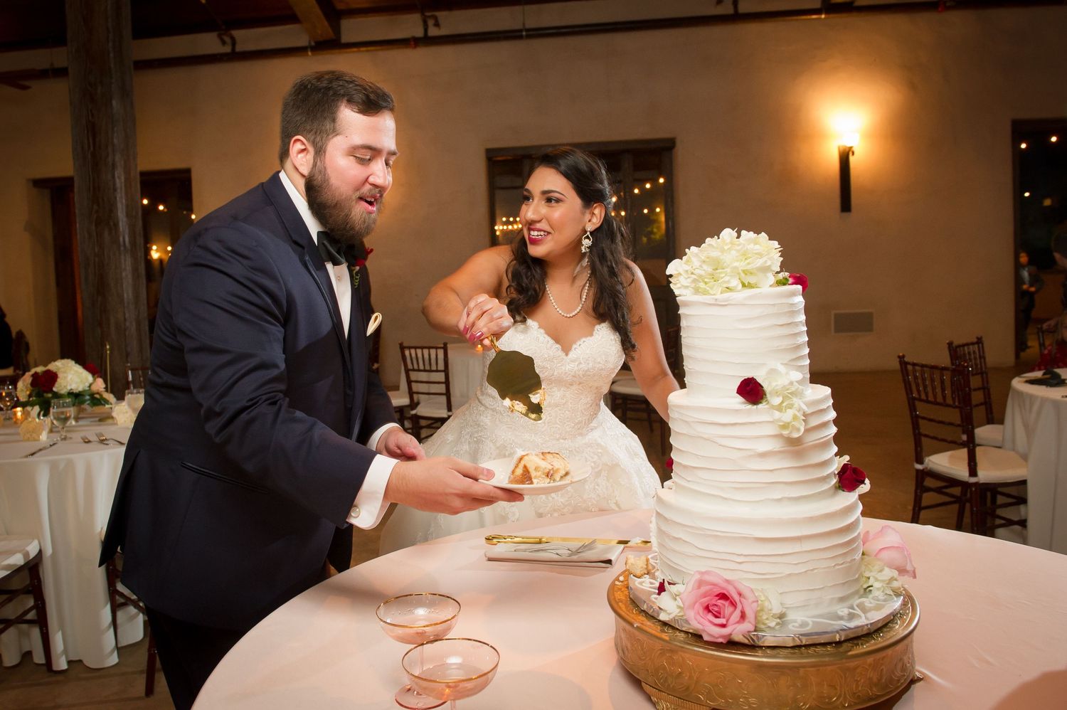 A couple shares their first bite of wedding cake together during an elegant indoor reception.