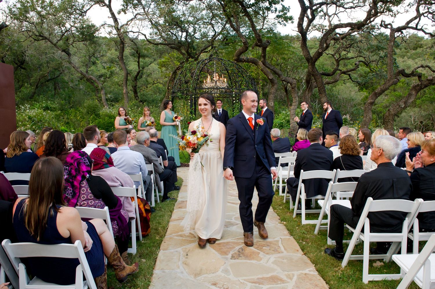 Outdoor wedding ceremony setup with white chairs and natural landscaping at a garden venue.