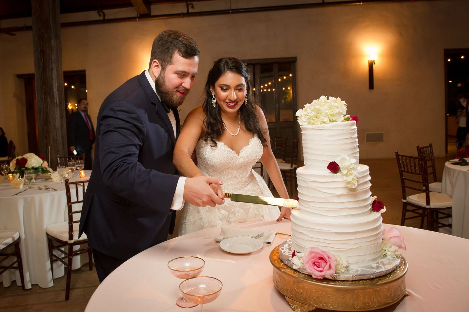 Wedding couple cuts their elegant white tiered cake during reception celebration.