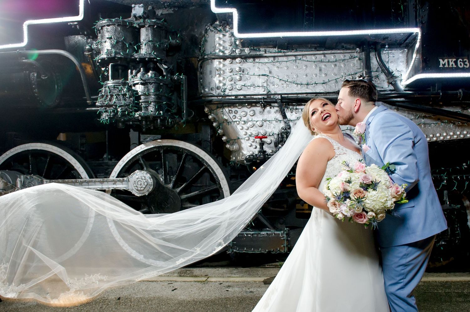 Flowing white wedding dress and veil create movement against dark train background.