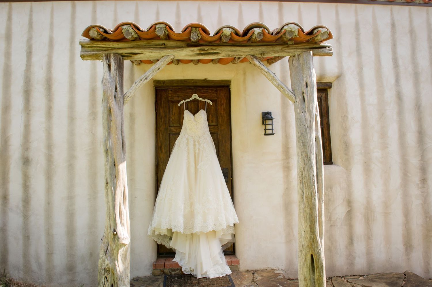 Wedding dress hangs elegantly against white curtained background.