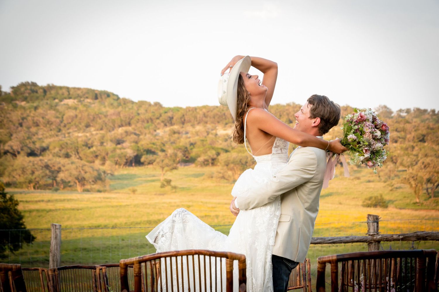 Wedding couple embracing on wooden deck overlooking scenic countryside views.