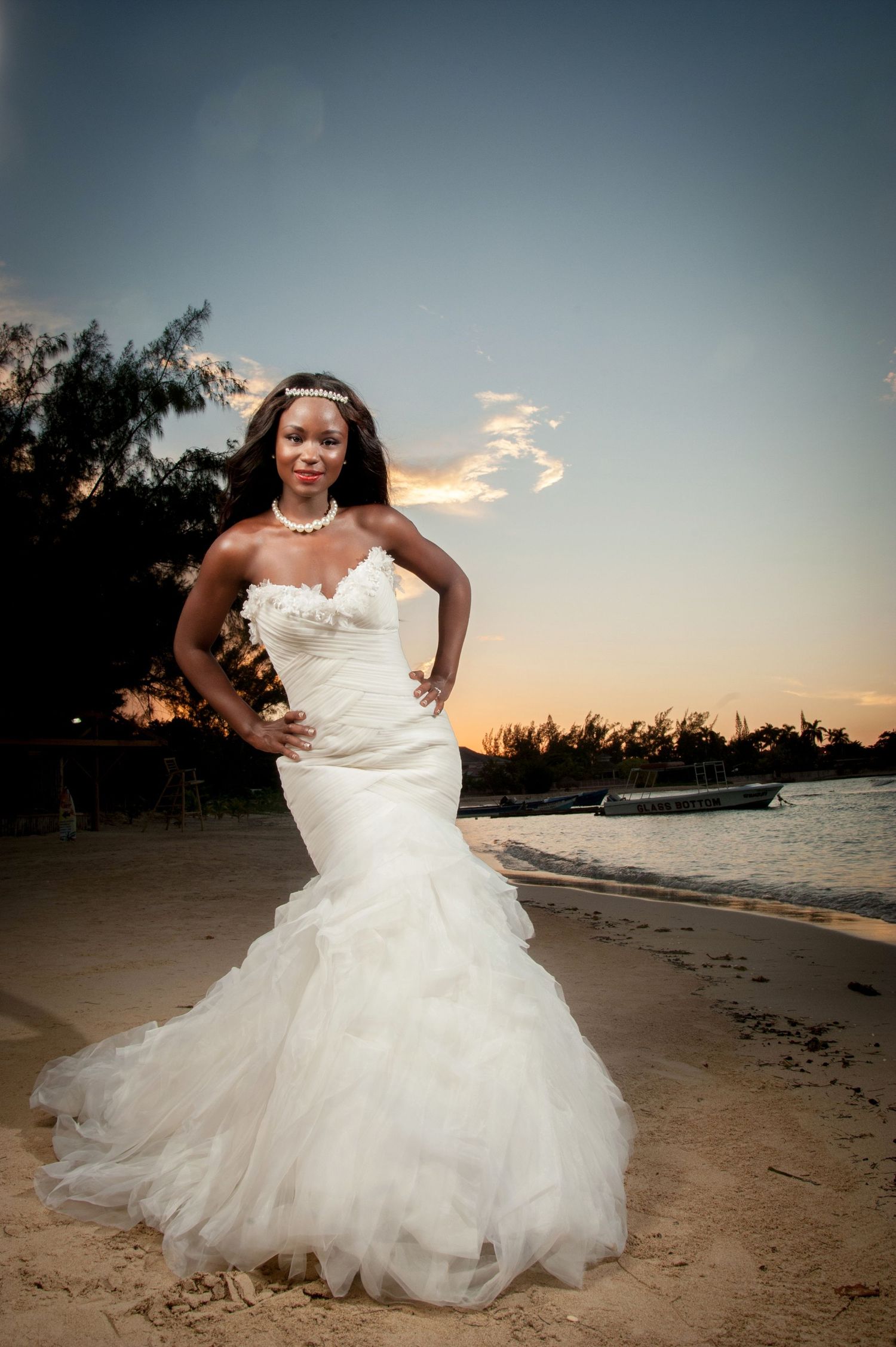 A bride in a white wedding gown poses gracefully on a sandy beach at sunset.