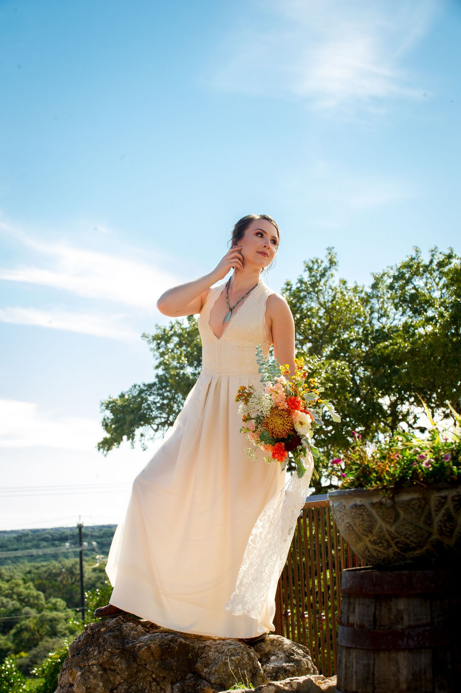 A bride in a flowing white dress poses gracefully against a scenic hilltop backdrop during golden hour.