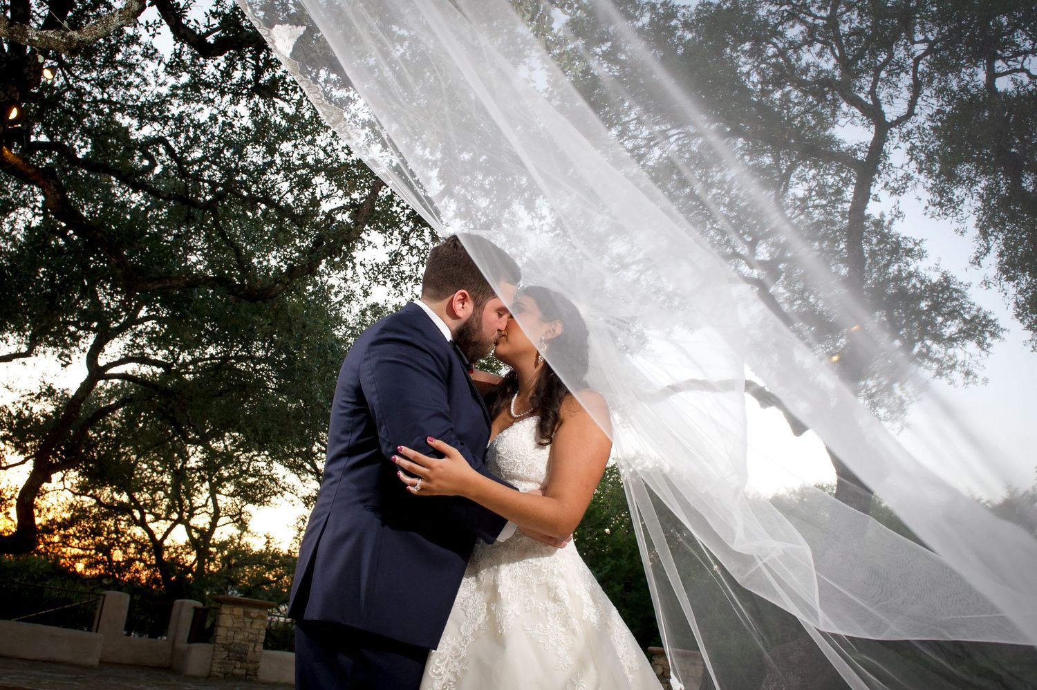 Romantic wedding portraits captured outdoors with flowing veil in golden evening light.