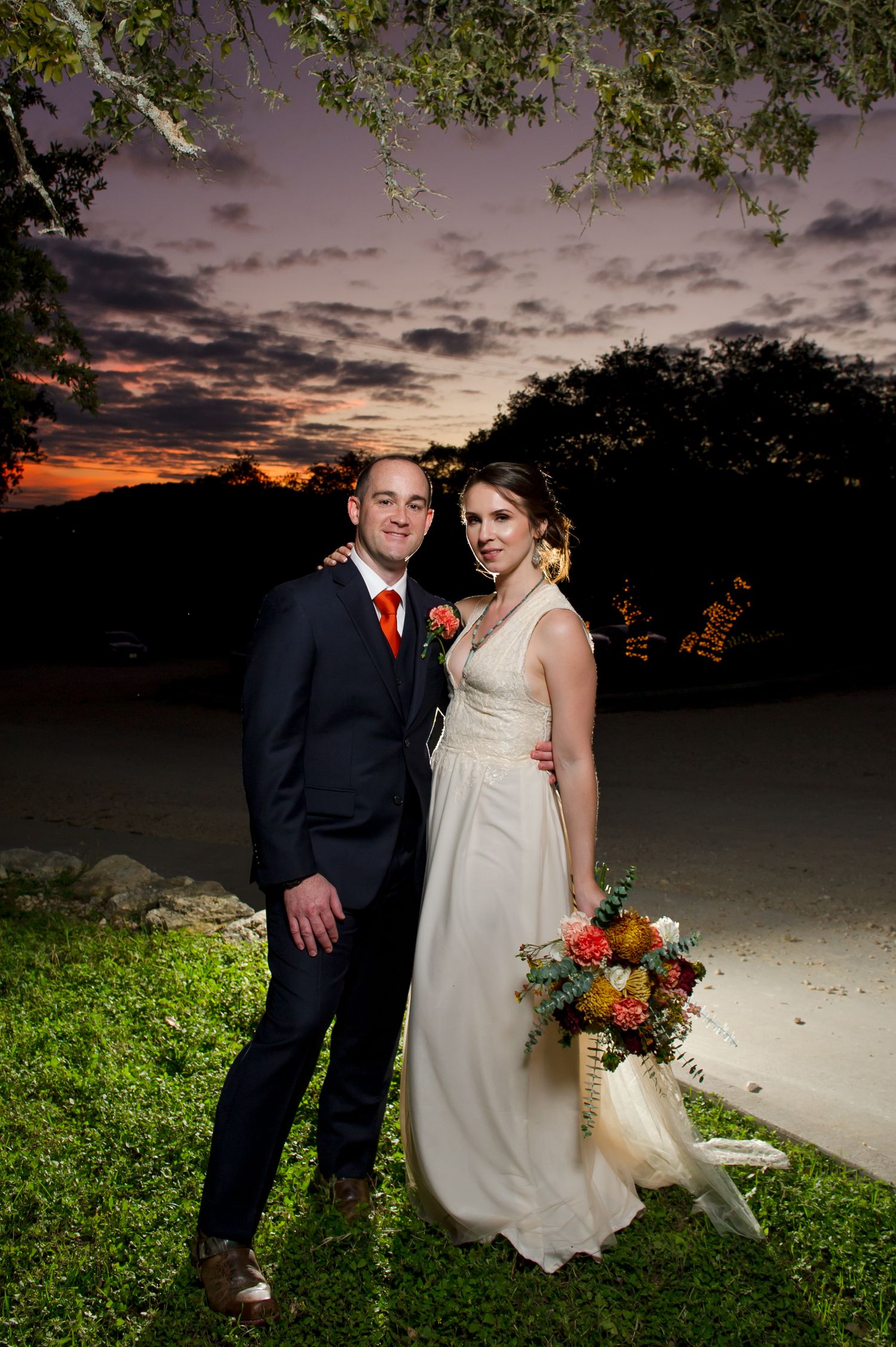 A couple poses for romantic sunset wedding photos on a grassy hill with dramatic cloudy skies.