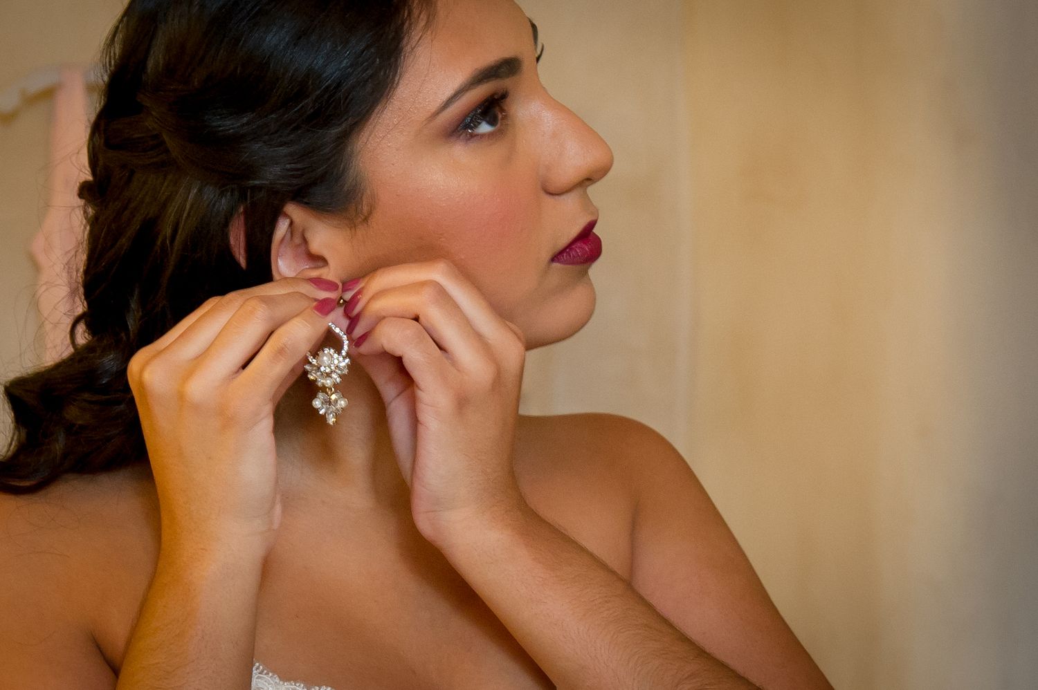 Close up of someone putting on elegant crystal drop earrings with red lipstick and dark hair.