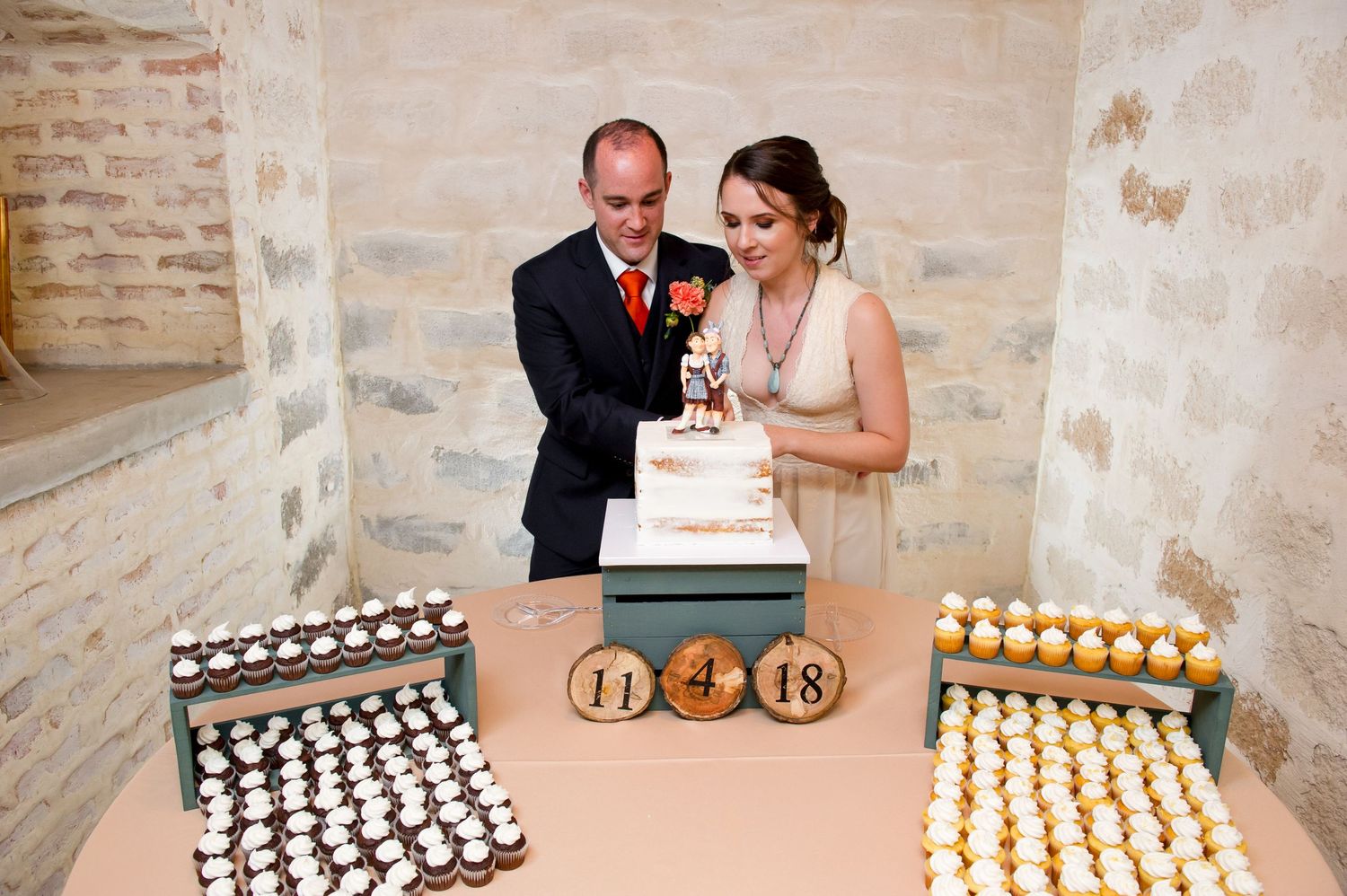 Wedding reception dessert table features rows of black and white cupcakes with gold number decorations at a rustic venue.