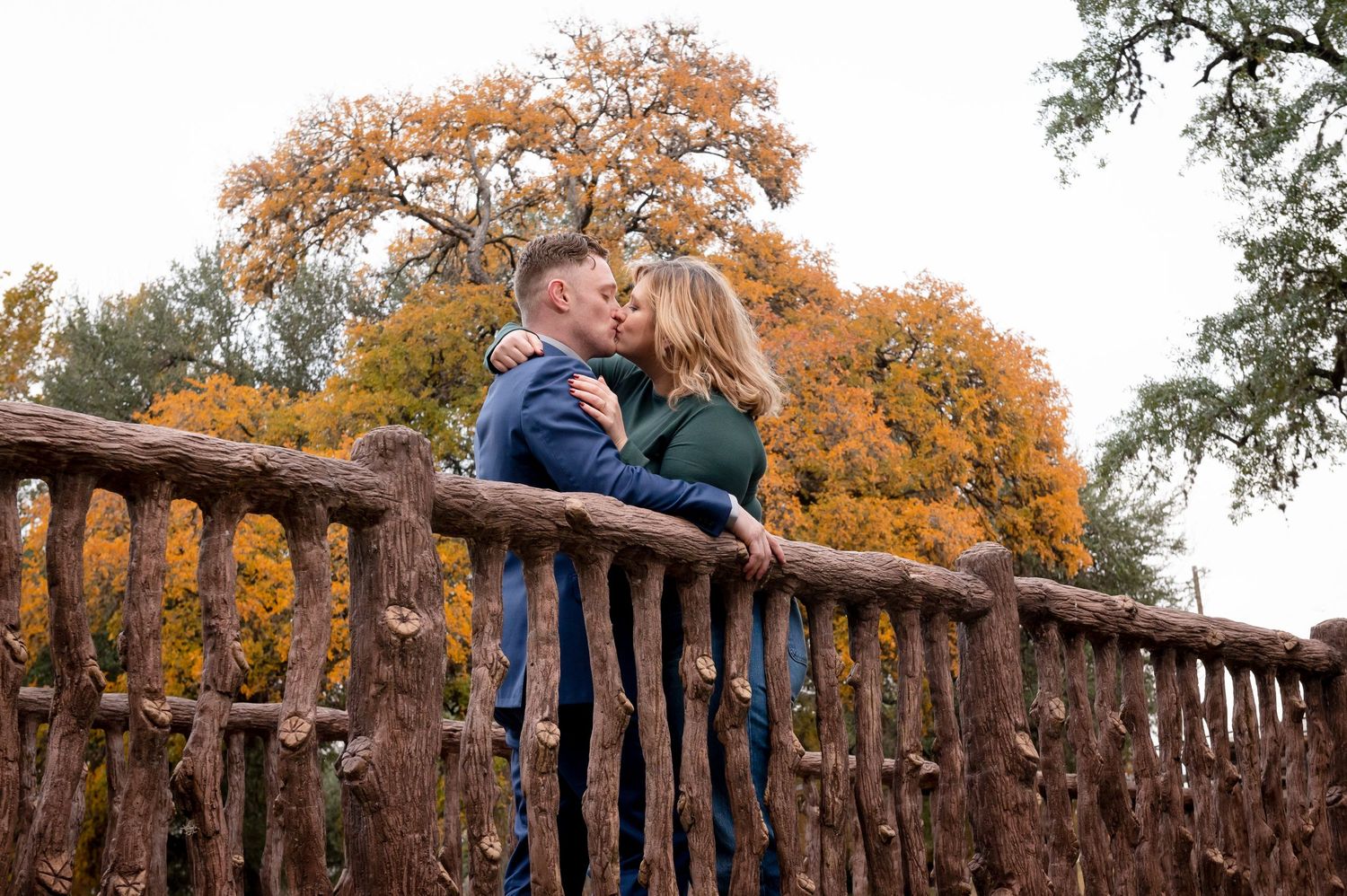 A romantic embrace on a rustic wooden bridge with golden fall foliage in the background.
