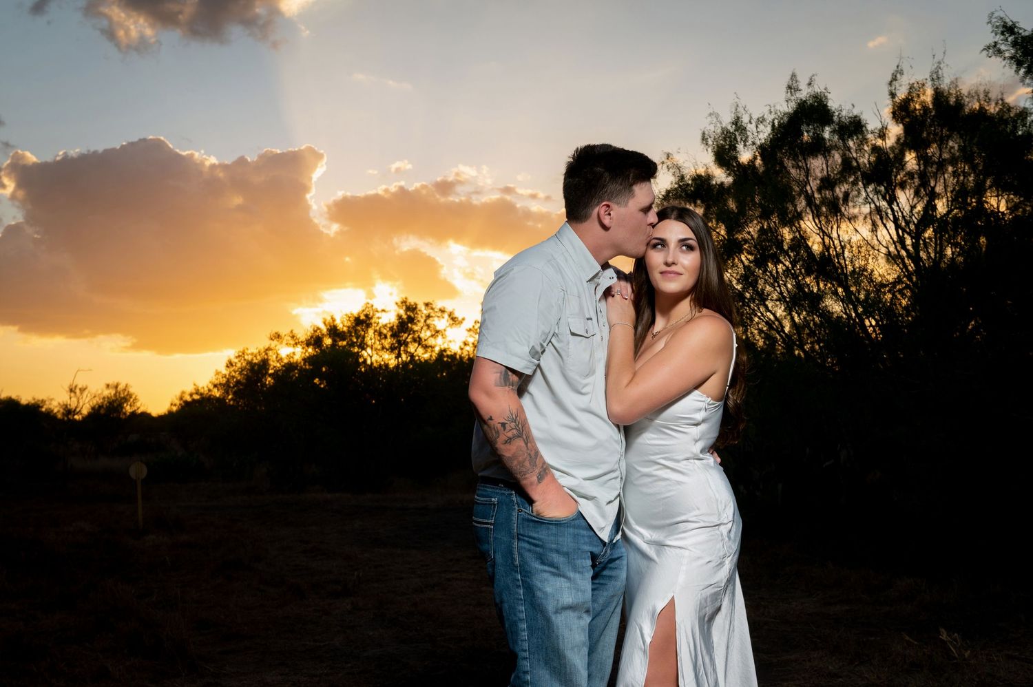Romantic sunset engagement photo with dramatic orange and pink sky.
