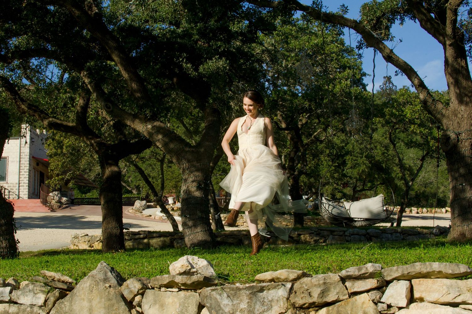 A bride in a white wedding dress poses gracefully on a rustic stone wall surrounded by lush greenery.