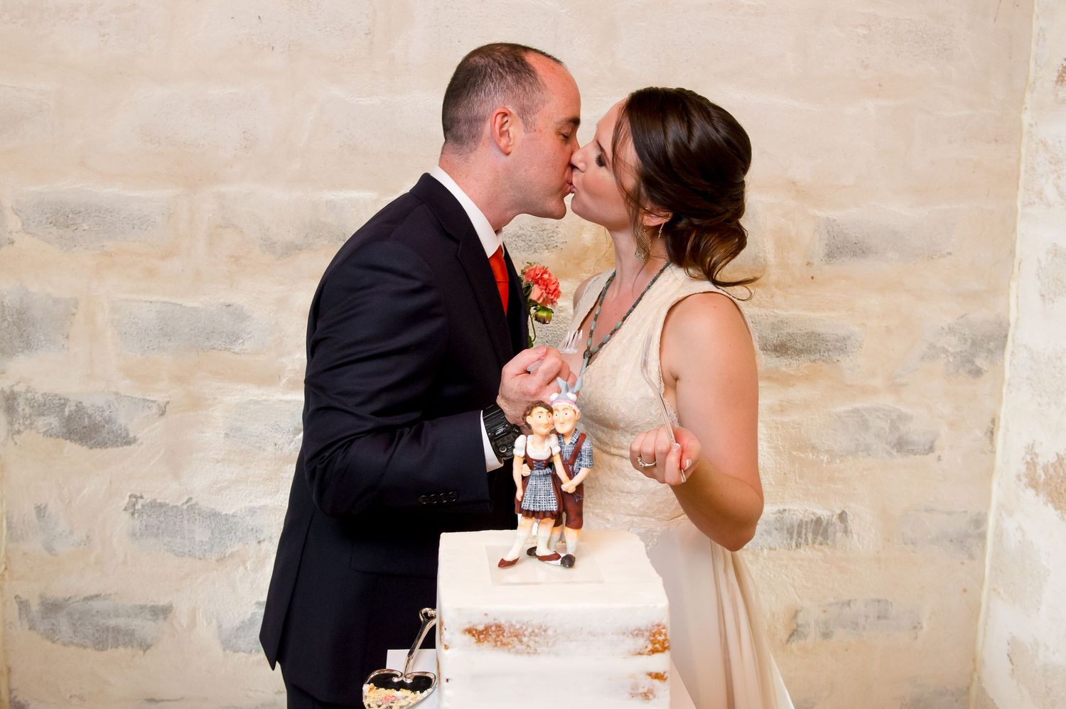 Newlywed couple shares a sweet moment while cutting their elegant white wedding cake together at their reception.