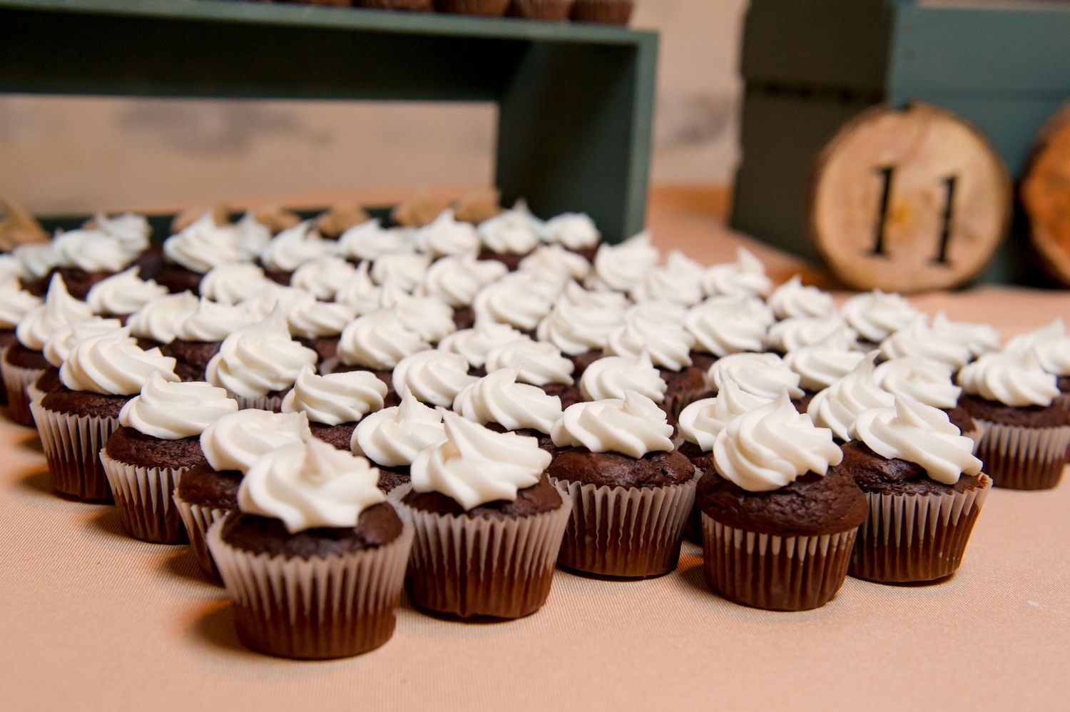 Rows of chocolate cupcakes topped with white frosting displayed at a wedding reception.