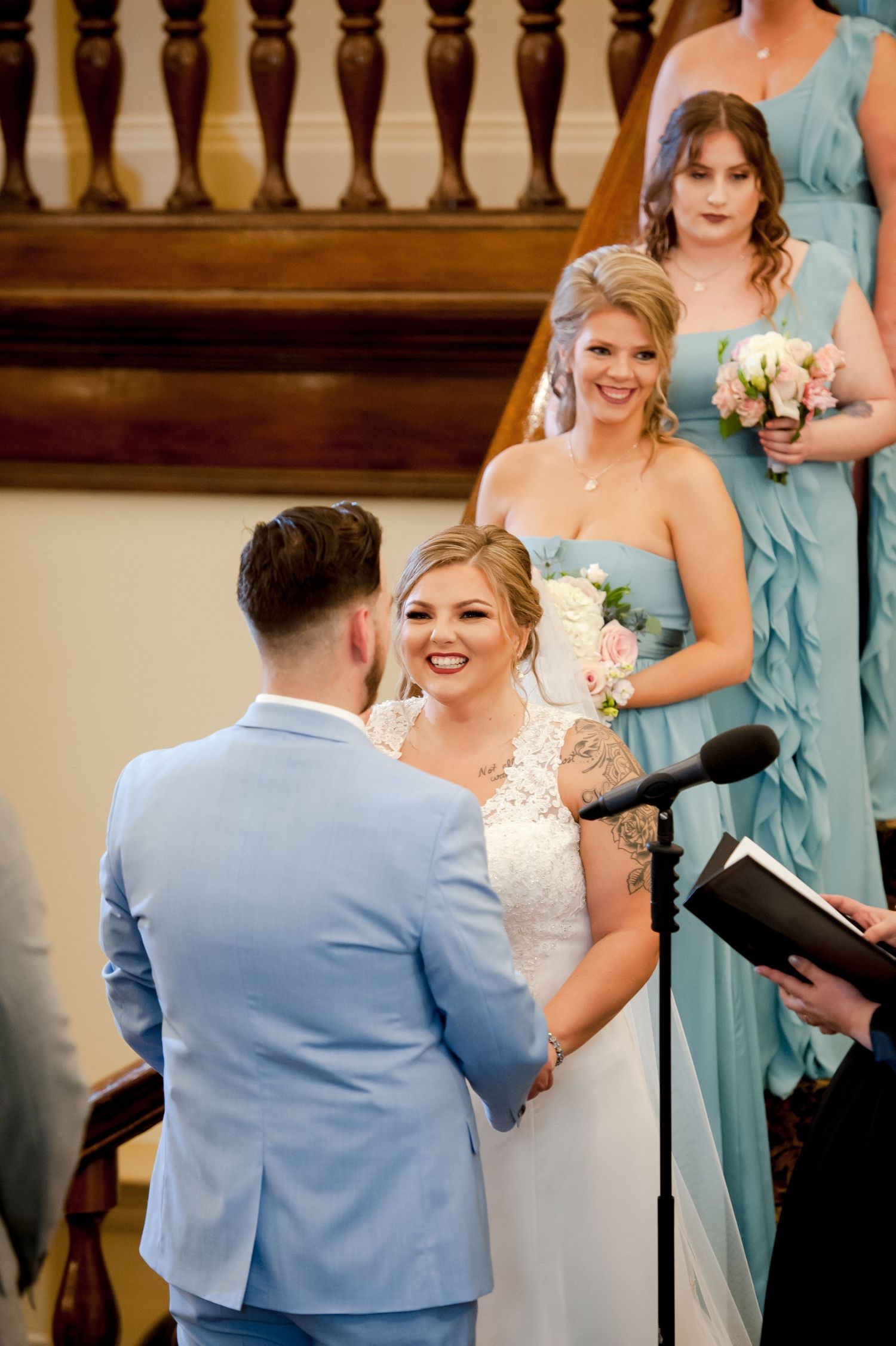 Wedding ceremony with attendants in light blue attire exchanging rings at an indoor venue.