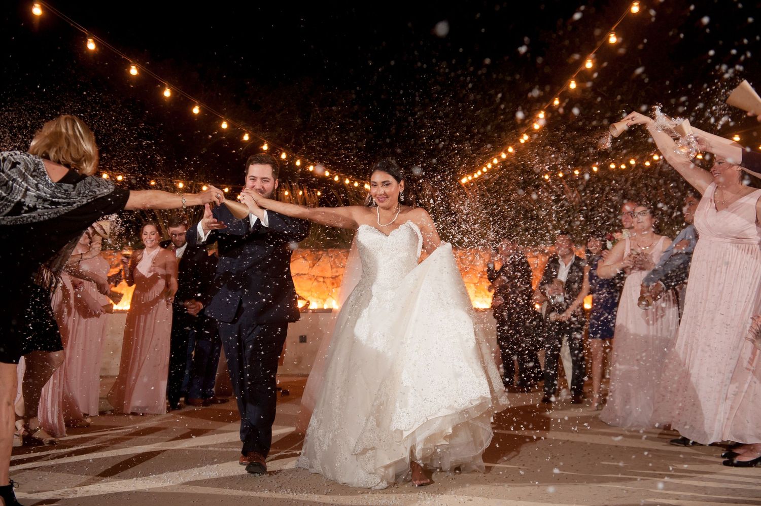 Wedding guests celebrate under string lights during an outdoor evening reception.