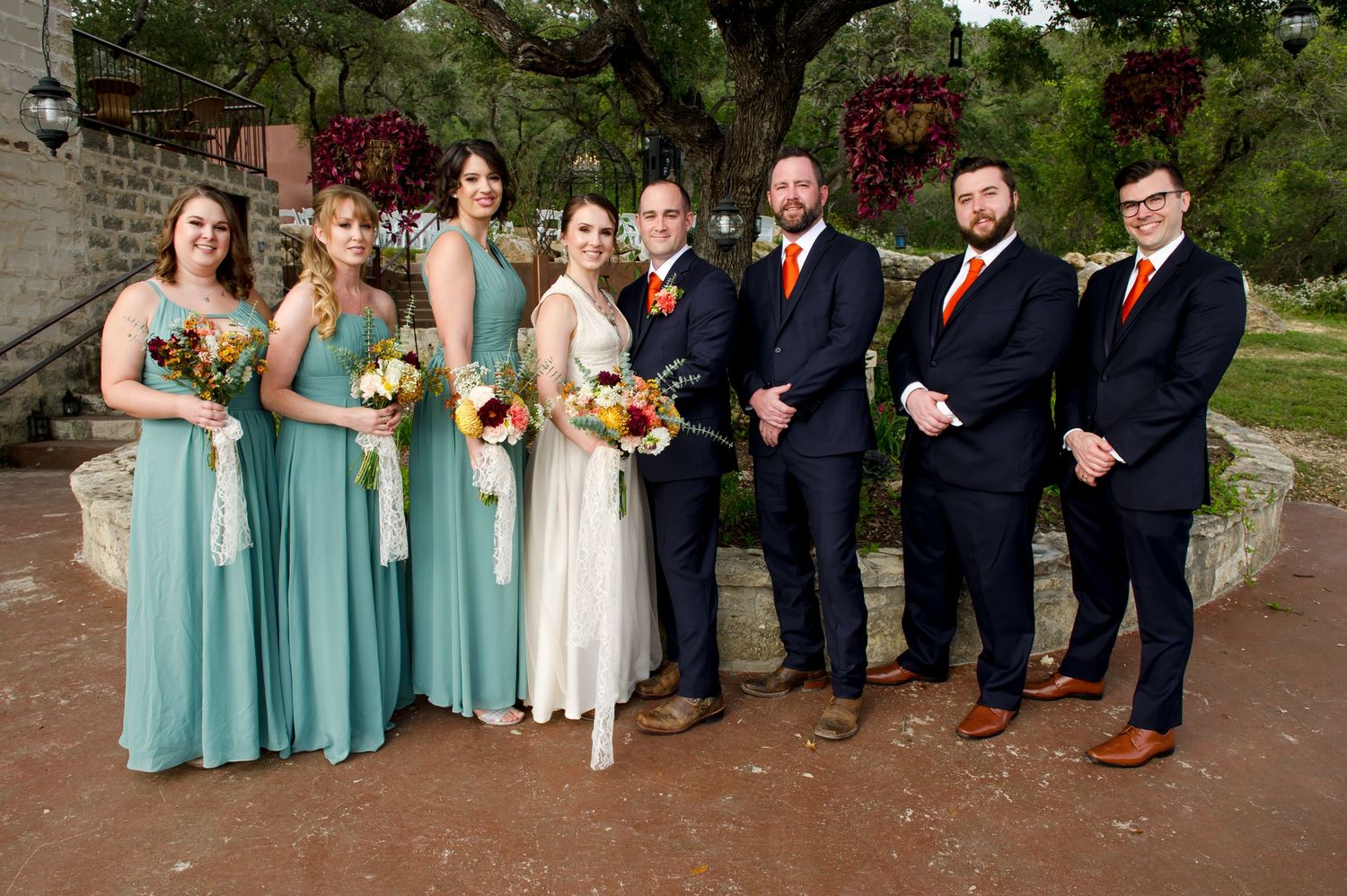 Wedding party in navy suits and mint green dresses pose together on stone steps outdoors.