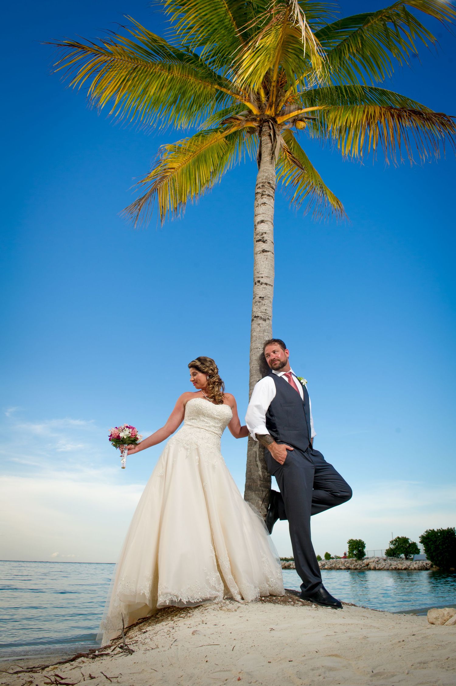 Beach wedding photos with palm trees and ocean backdrop in tropical paradise setting.