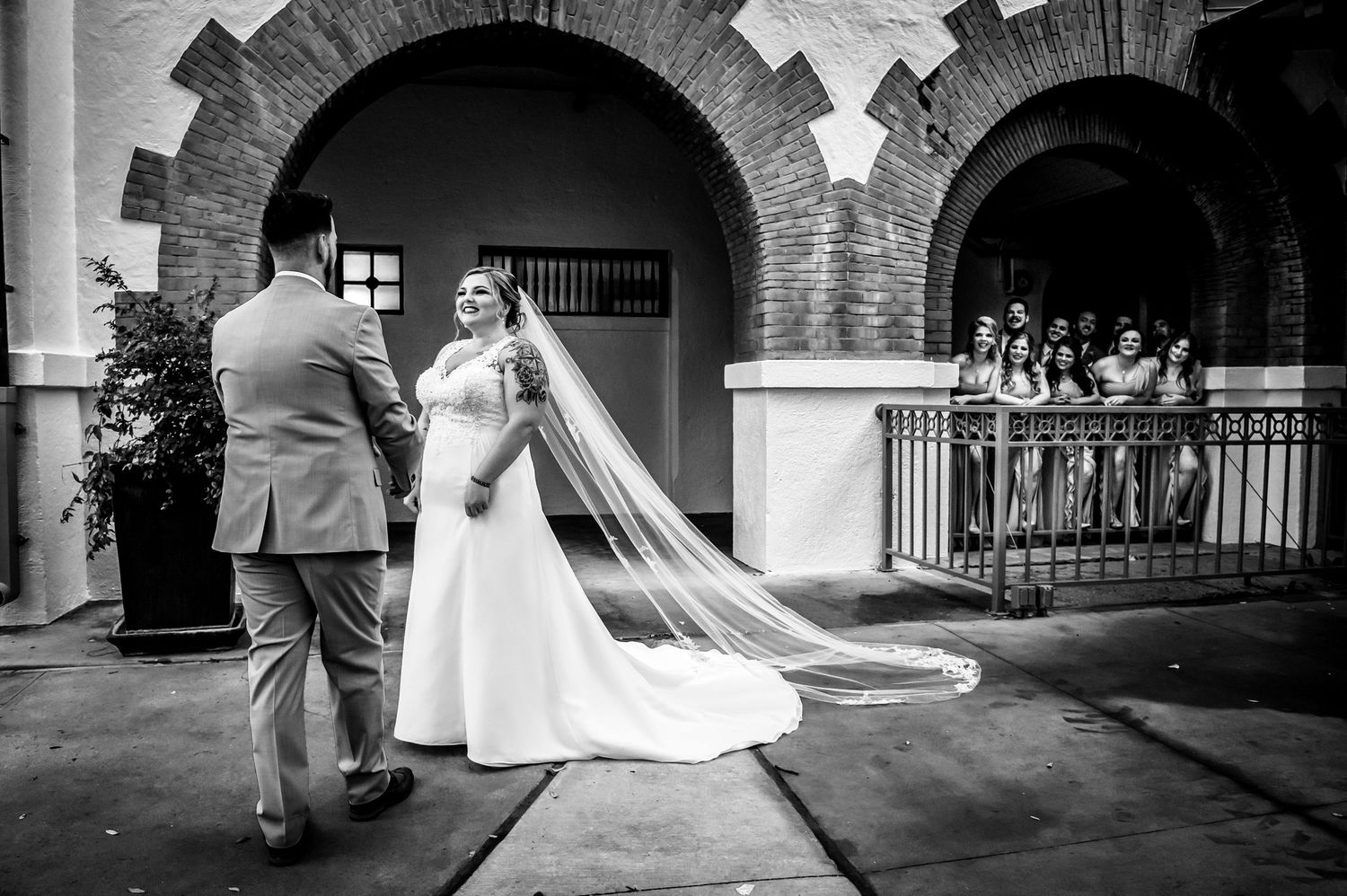 A wedding couple stands under ornate stone archways at a historic venue.