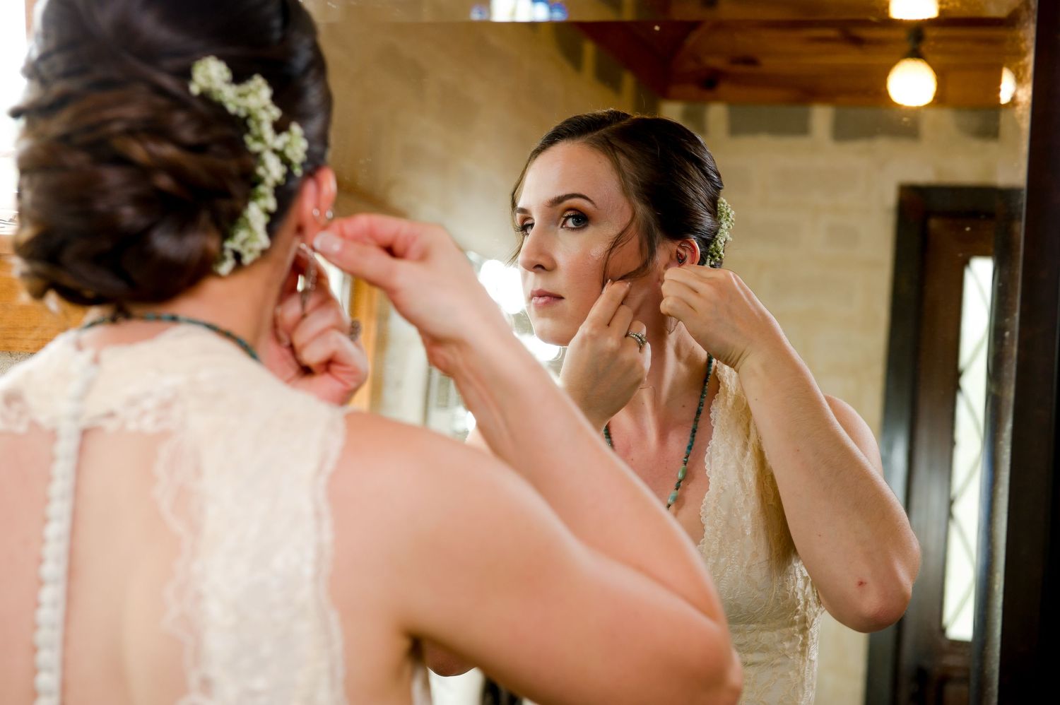 Two people getting ready in formal attire while putting on earrings in a warmly lit room.