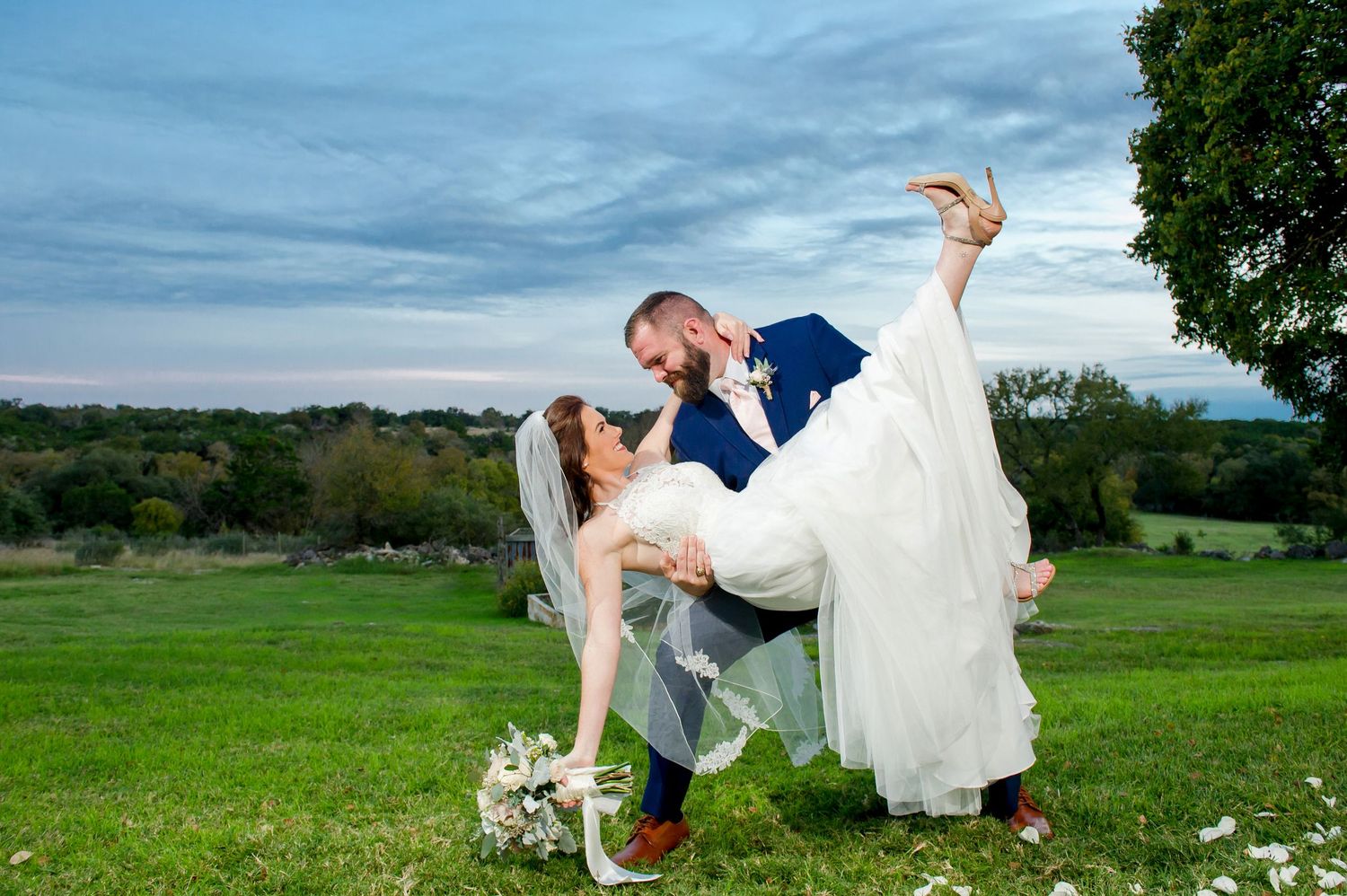 Wedding couple poses playfully in a field of wildflowers at sunset with dramatic clouds in the background.