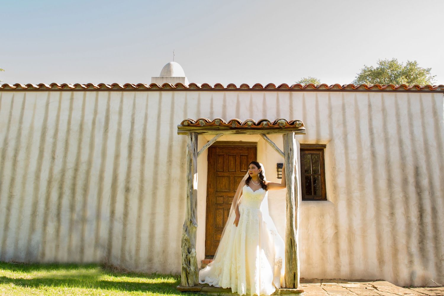 White Spanish colonial style building exterior with rustic wooden doors and terra cotta tile roof.