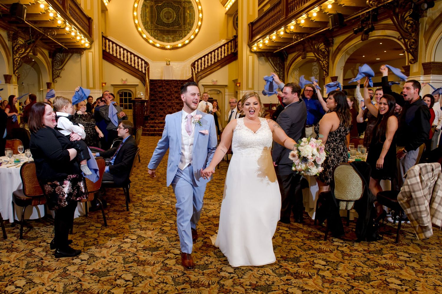 Happy couple walks through elegant venue with guests applauding.