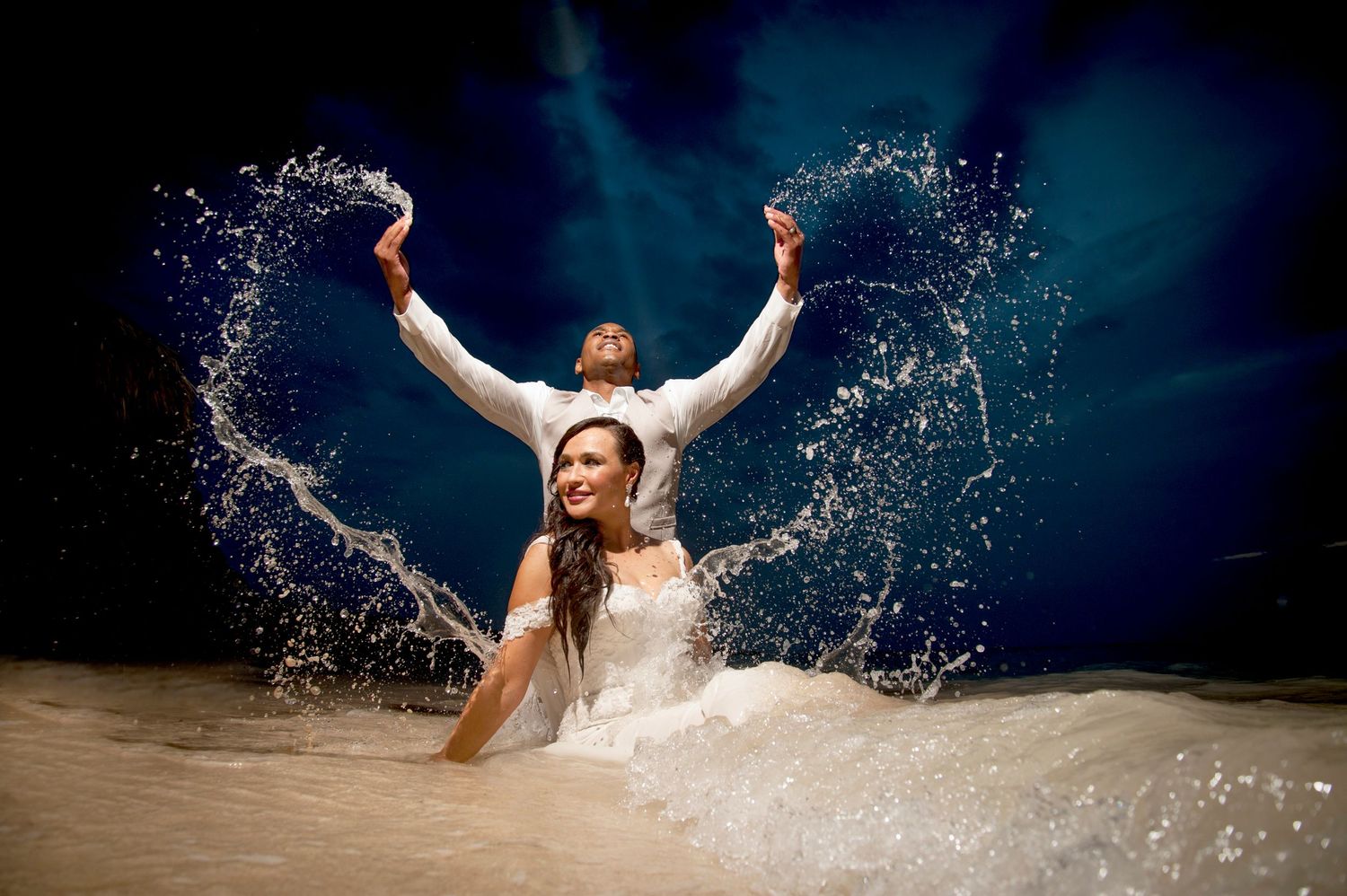 Bride in white dress creates dramatic splash in pool during underwater photo session.