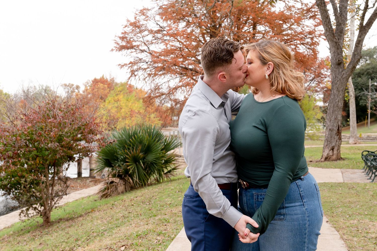 A romantic autumn moment shared between a couple on a grassy hill with fall foliage in the background.