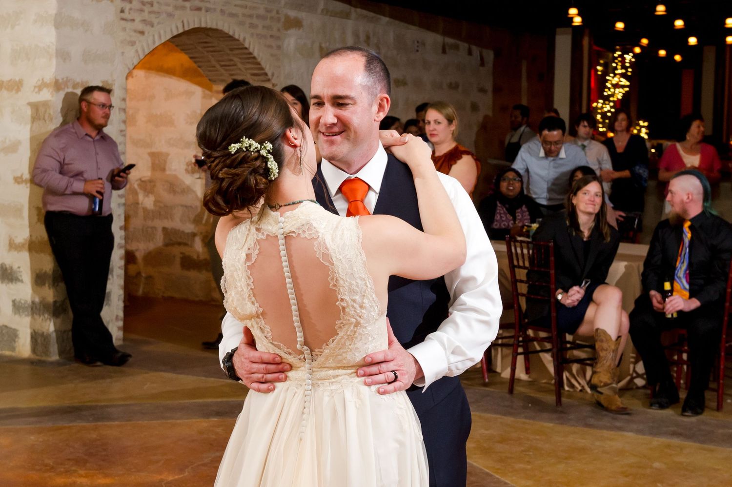A couple shares a romantic dance moment at their wedding reception in an elegant venue with twinkling lights.
