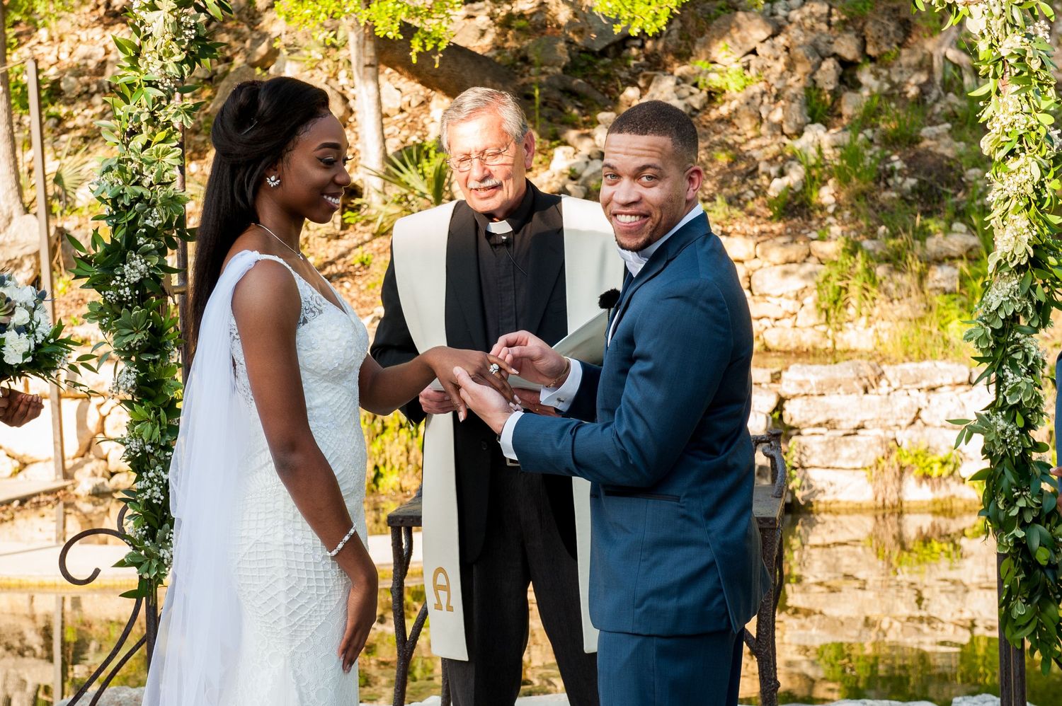 Wedding ceremony exchange of rings in front of stone wall with natural lighting.